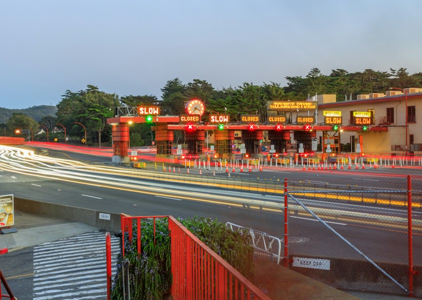 A toll plaza at dusk with vehicle light trails, representing a single gateway every model request passes through