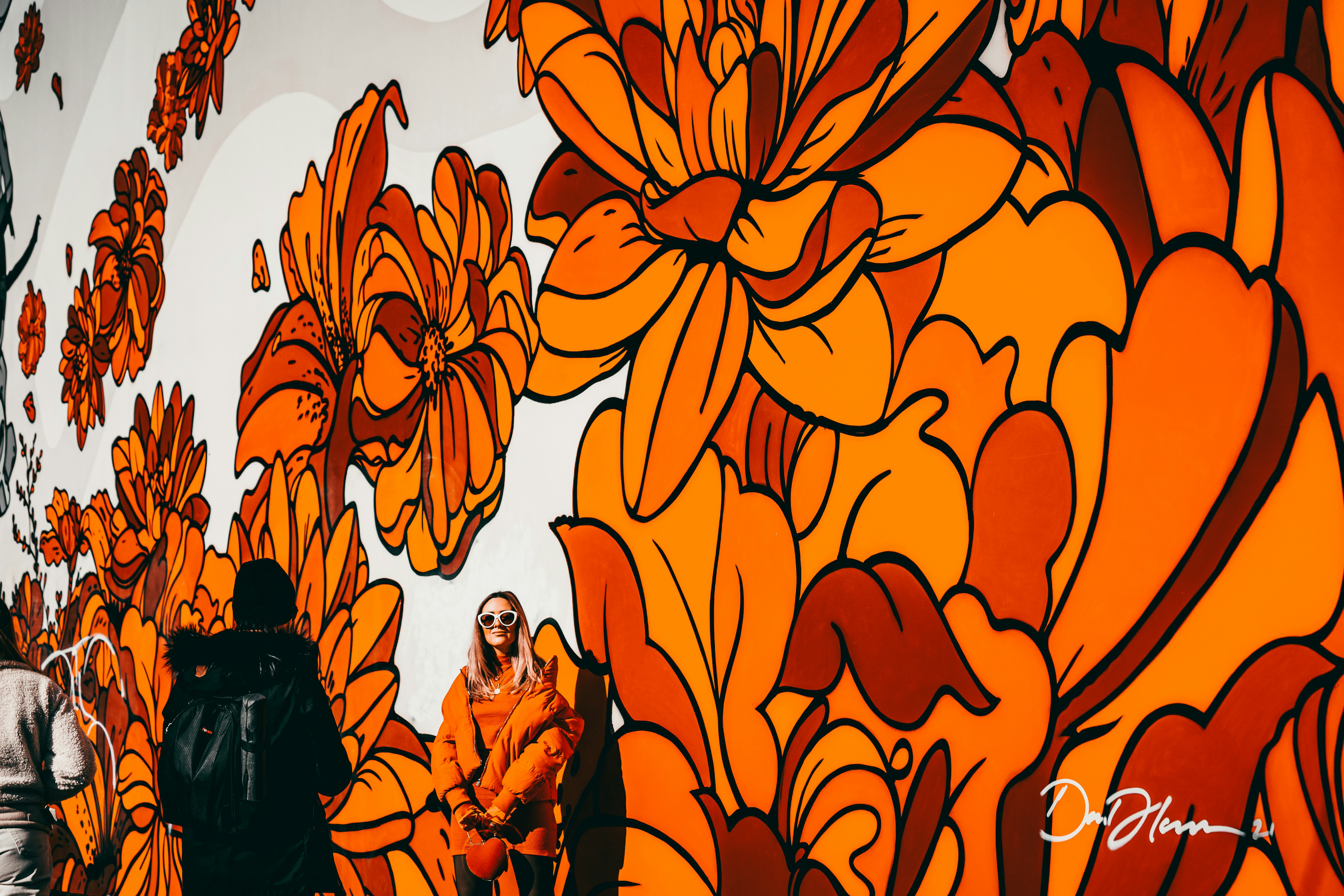 People walk past a vibrant floral mural with orange hues.