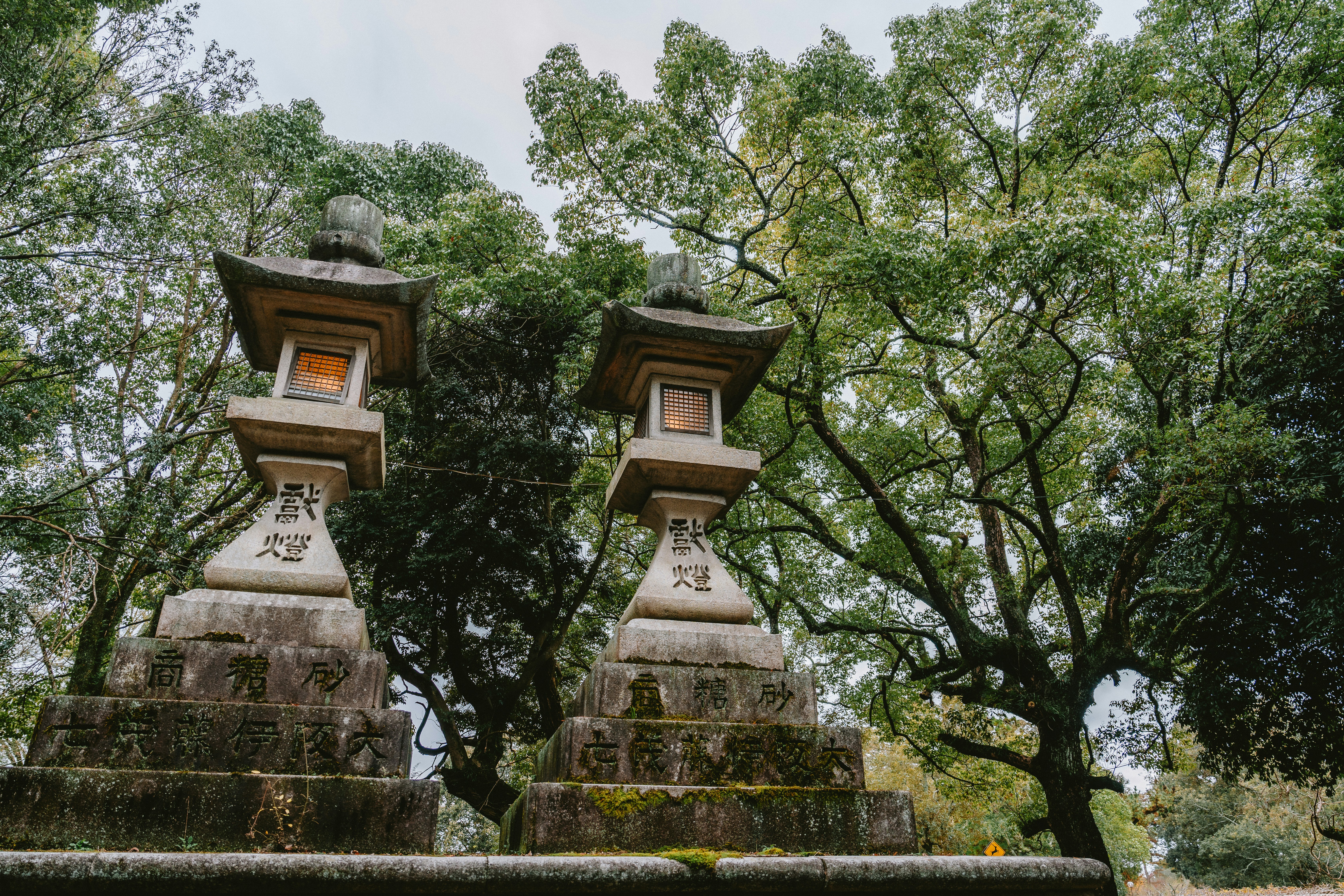 Two stone lanterns stand amidst lush green trees.
