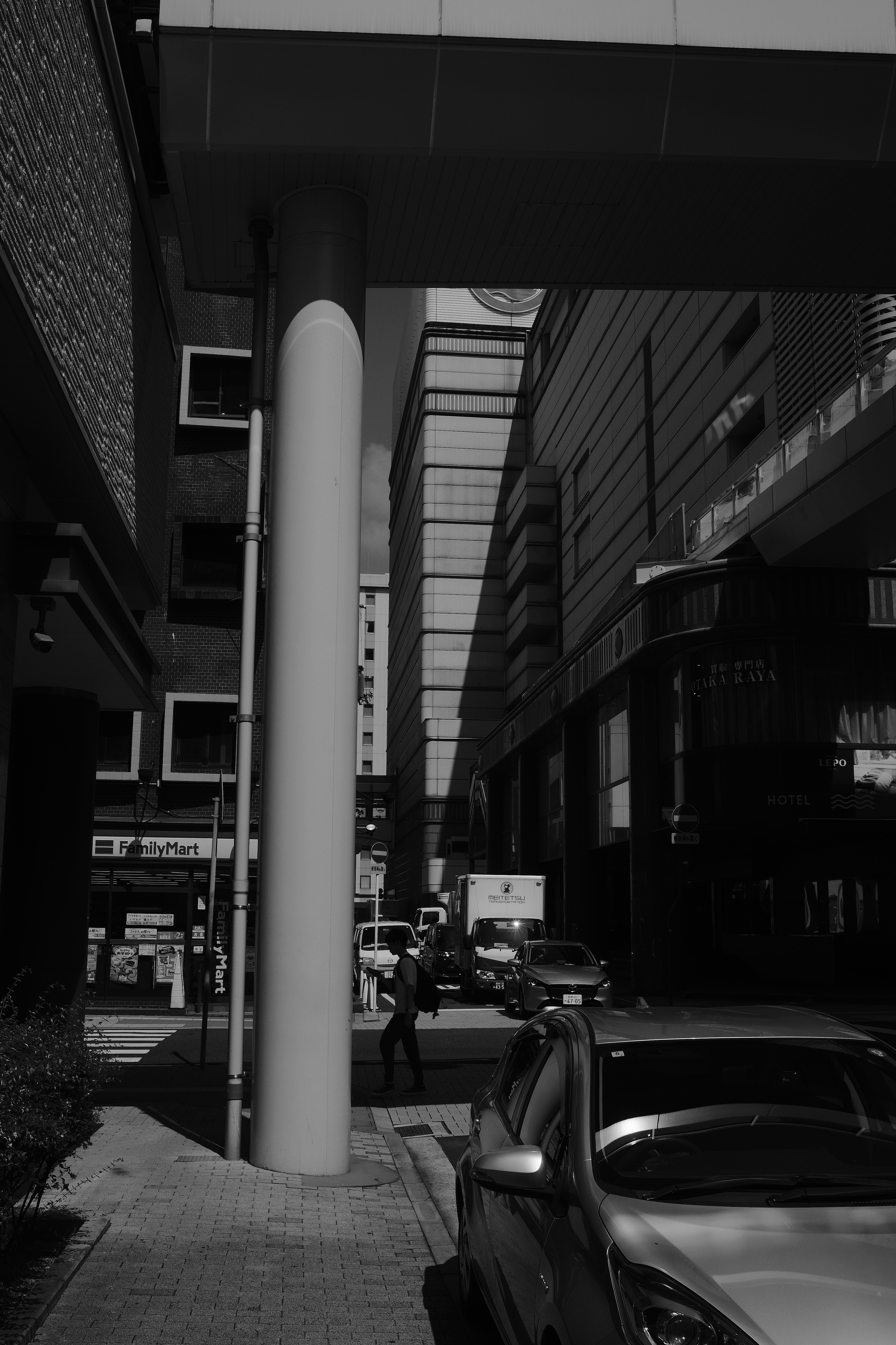 Man walks down a sunlit city street between buildings.