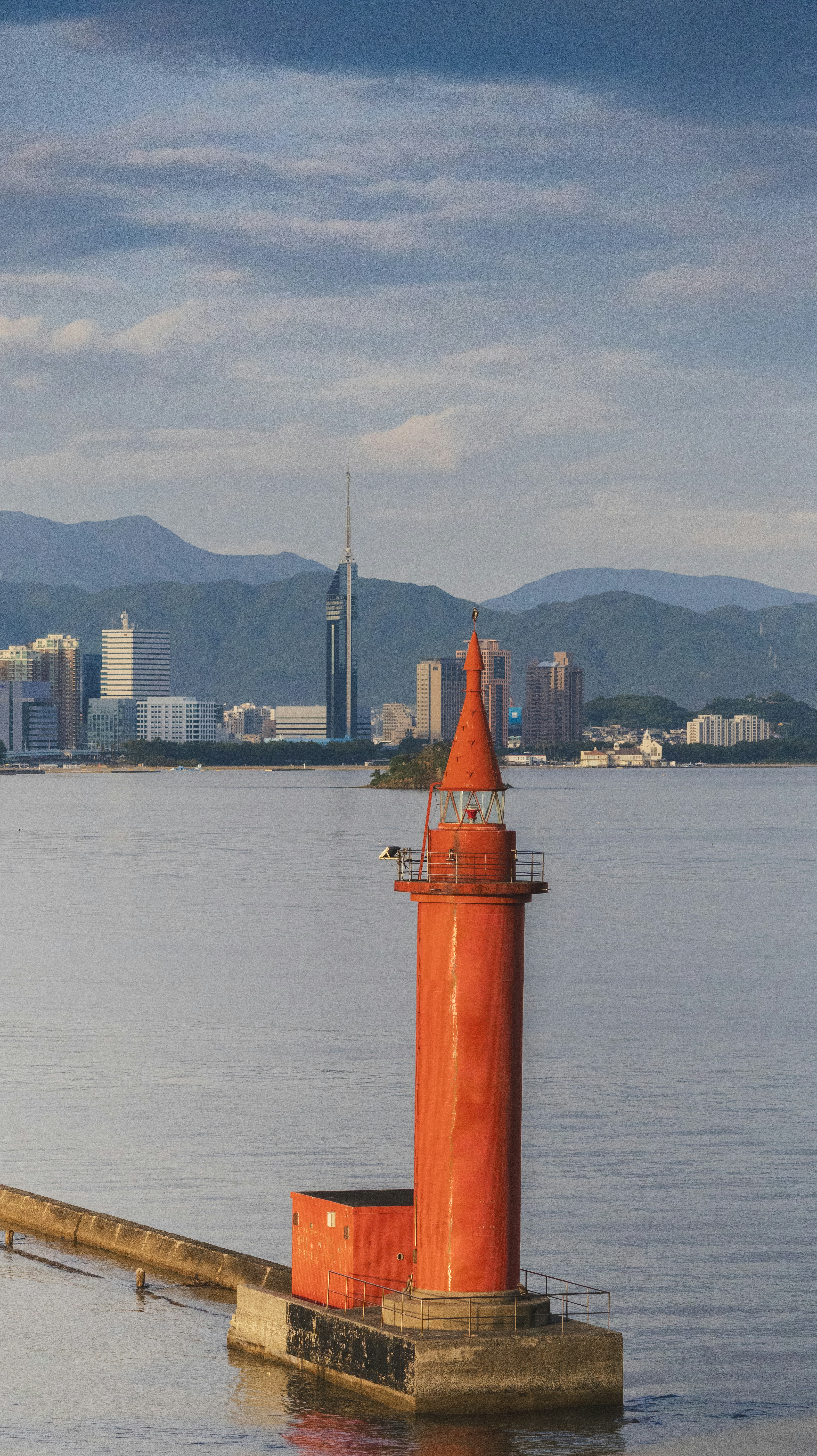 Red lighthouse on a pier with city skyline background.