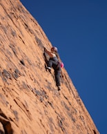 Woman rock climbing a steep orange cliff face