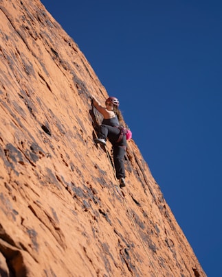 Woman rock climbing a steep orange cliff face