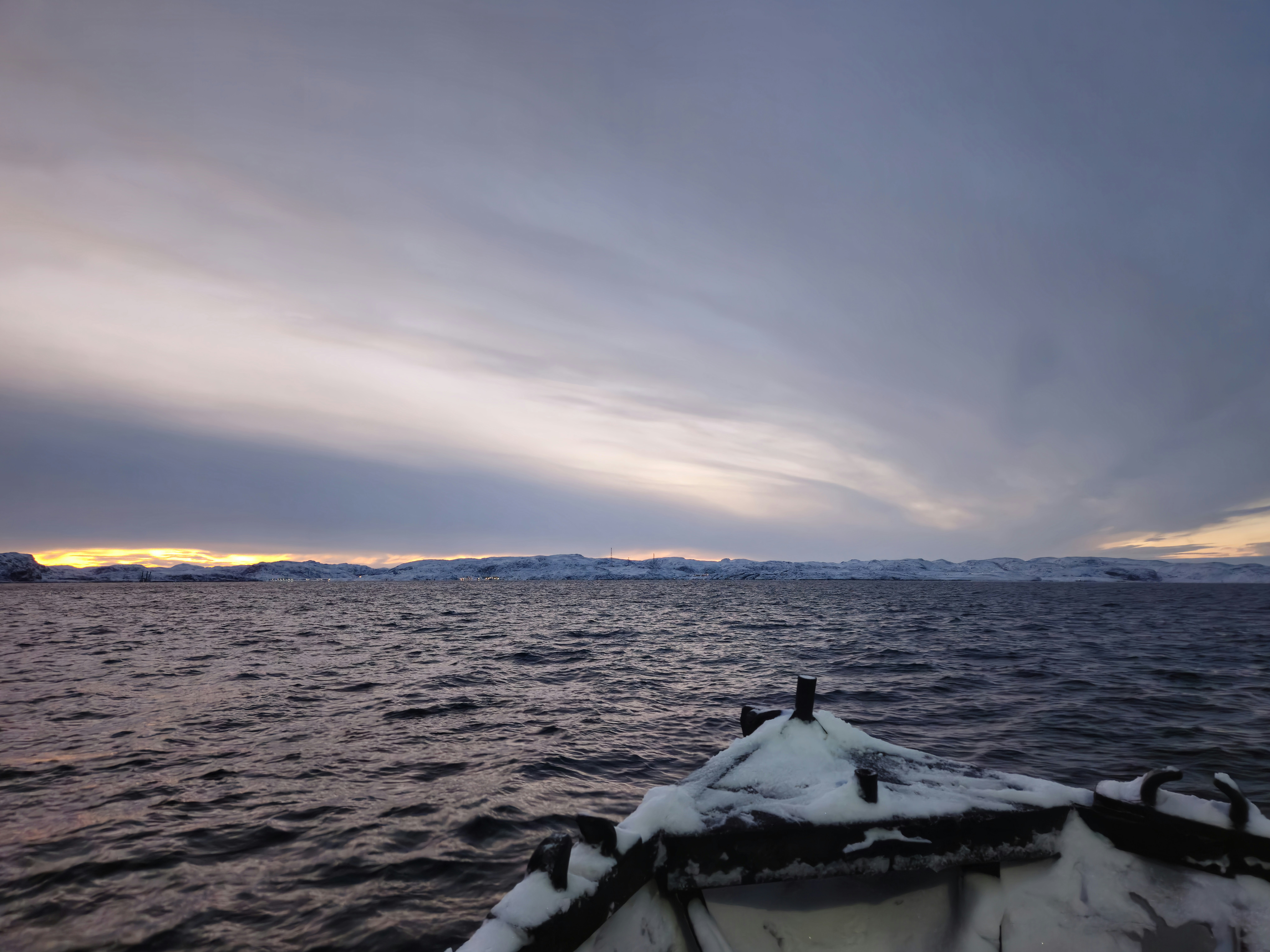 prua della barca innevata sull'acqua increspata sotto il cielo nuvoloso