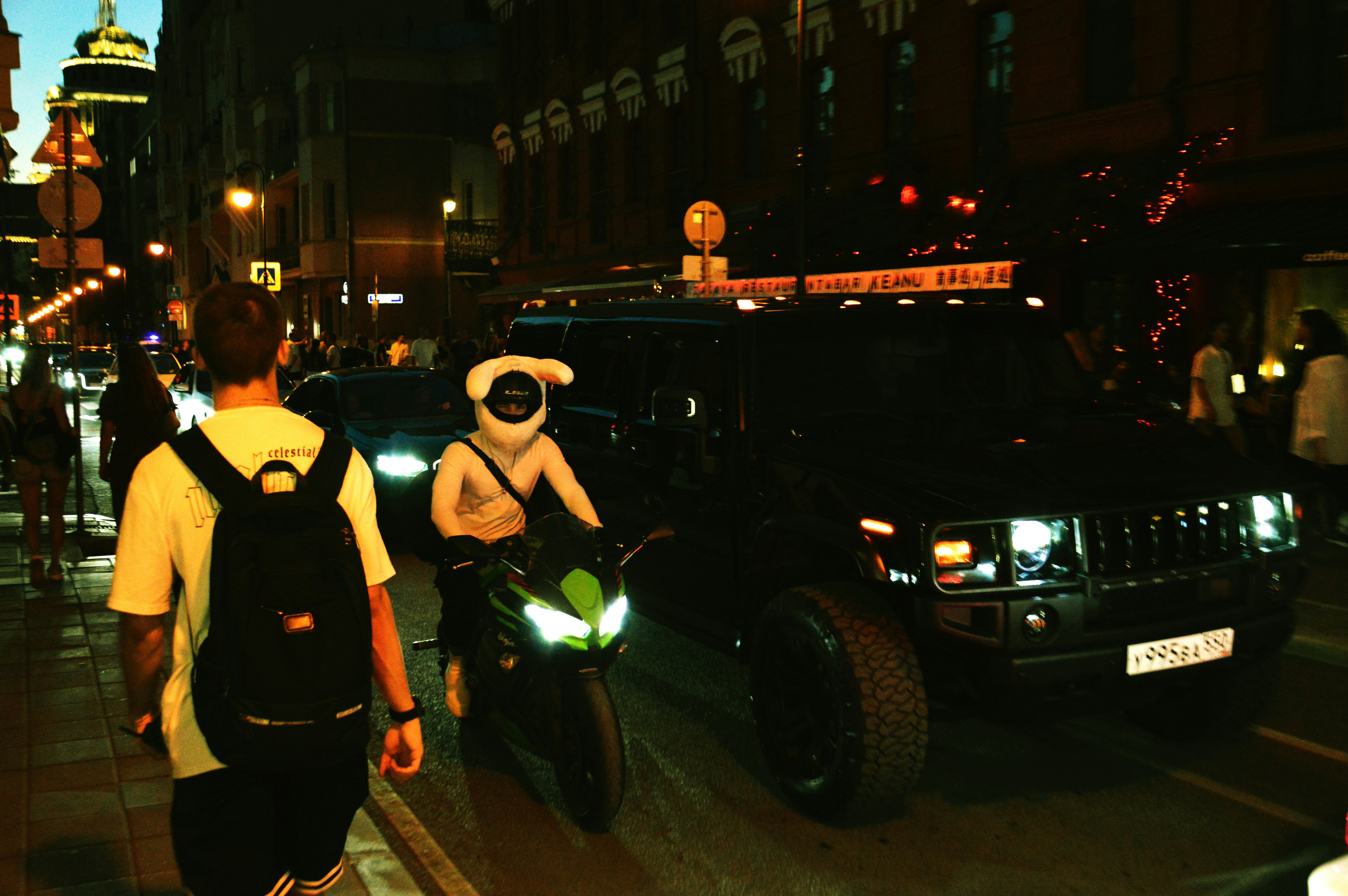 Motorcyclist in costume rides past a limousine at night.