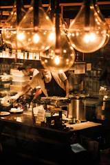 Chef preparing food behind a counter with warm lights.