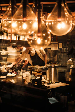 Chef preparing food behind a counter with warm lights.