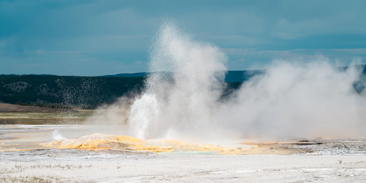A geyser erupting with steam against a blue sky in a geothermal landscape