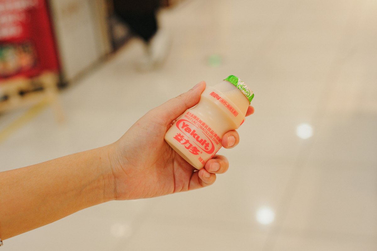 Yakult bao nhiêu calo: tay cầm một chai Yakult nắp xanh trong siêu thị