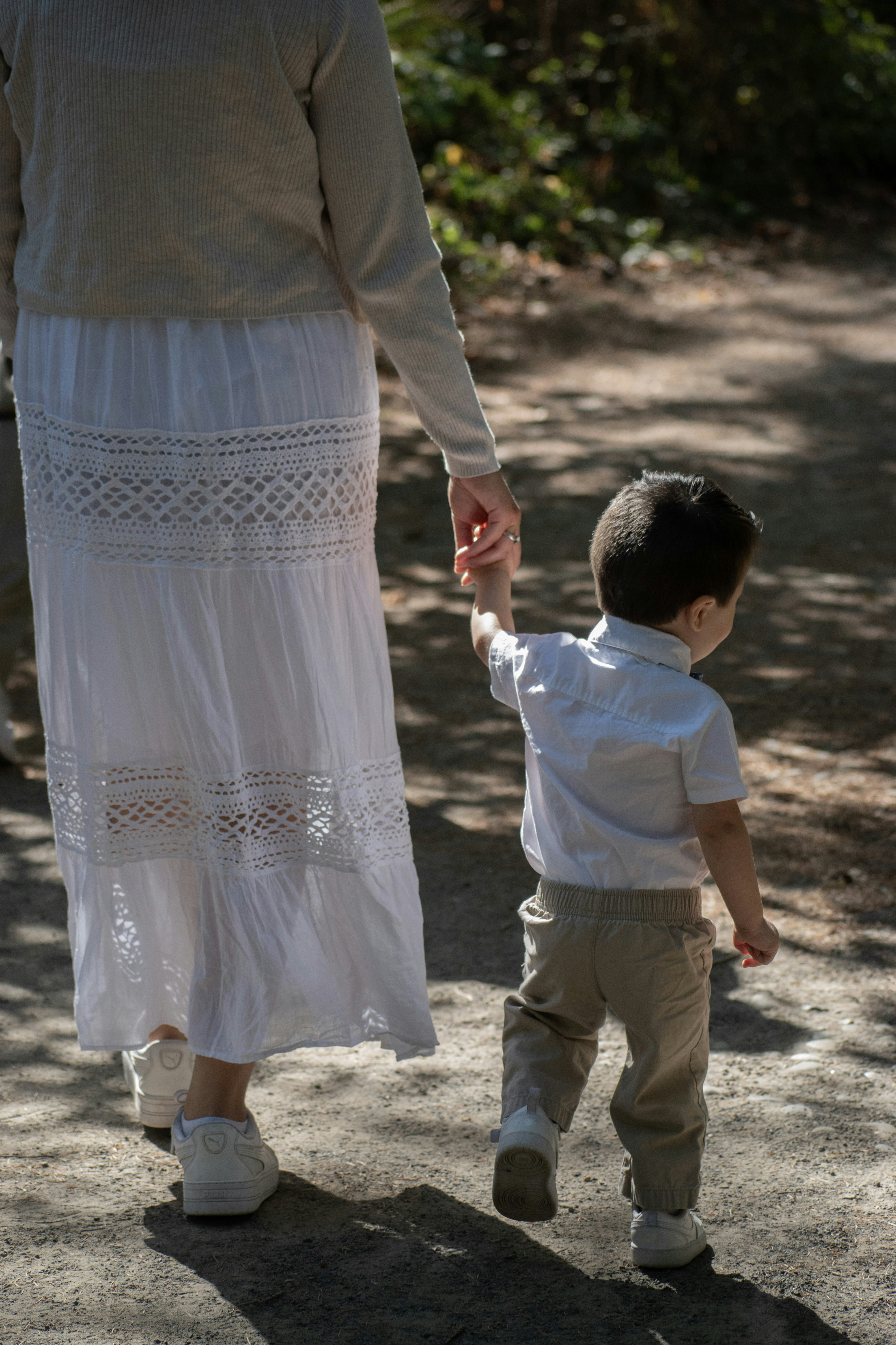 A woman holds a child's hand walking on a path.