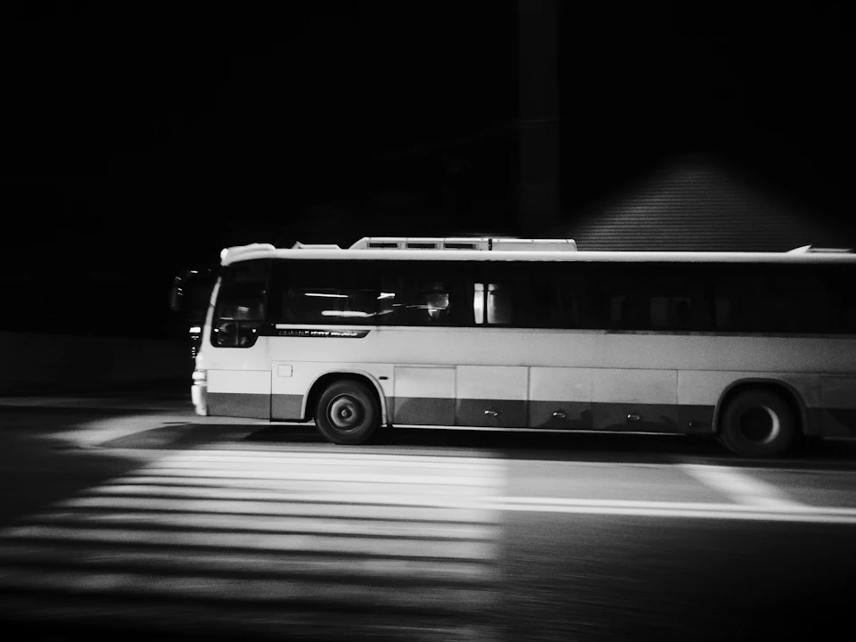 White bus travels down street at night with headlights illuminating the road ahead