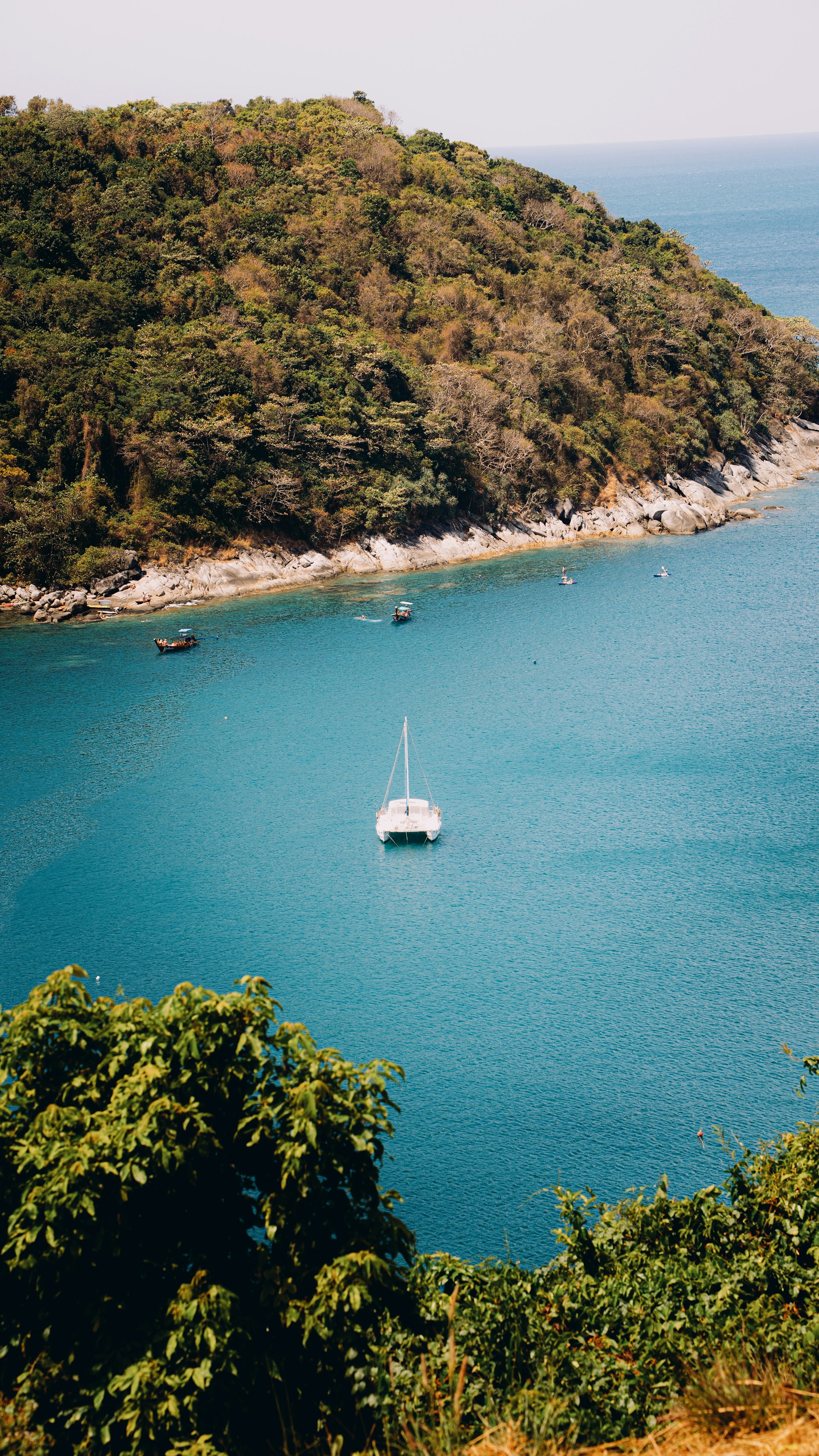 A white sailboat floats on a calm blue bay.