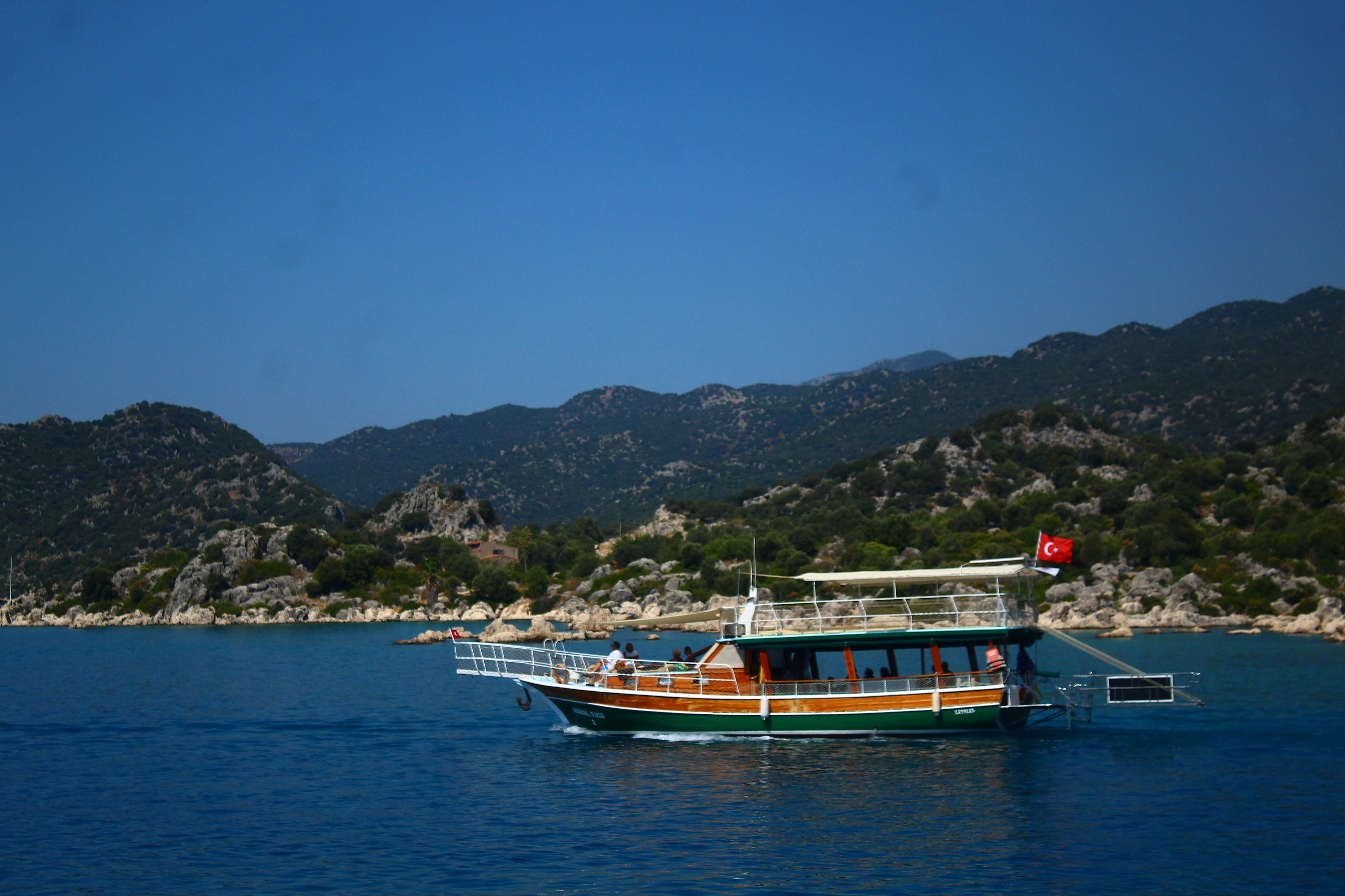 A boat sails on the blue sea near mountains.