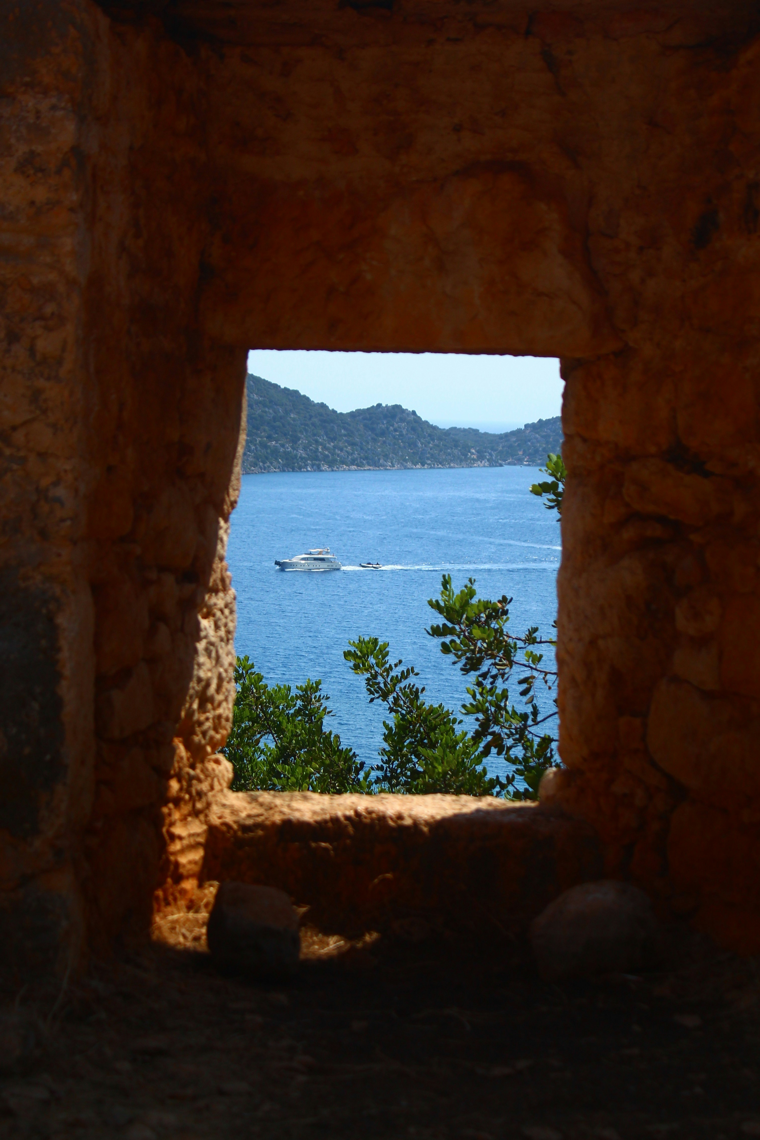 Yacht sailing on blue sea through stone window.
