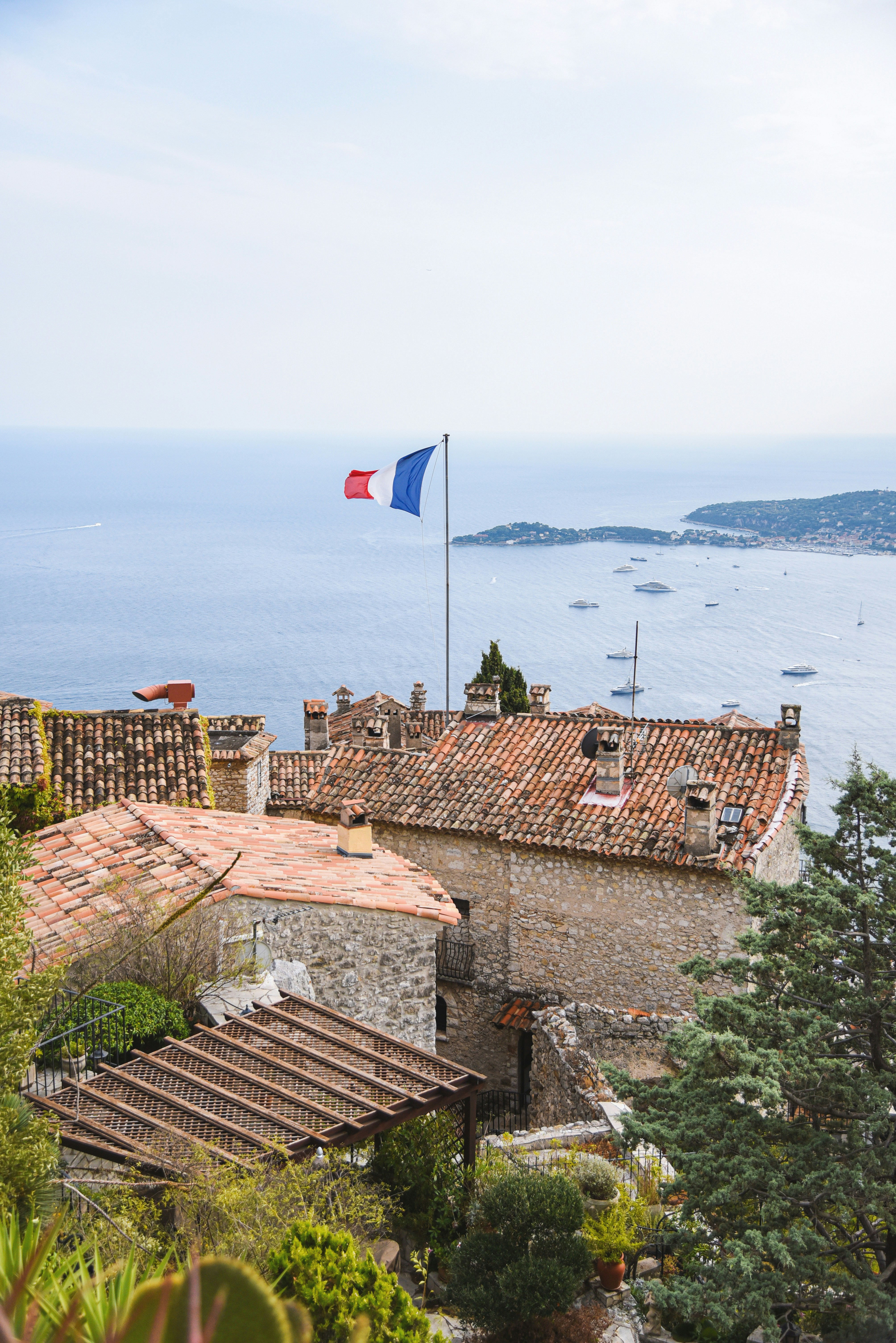 French flag flies over coastal village with boats.