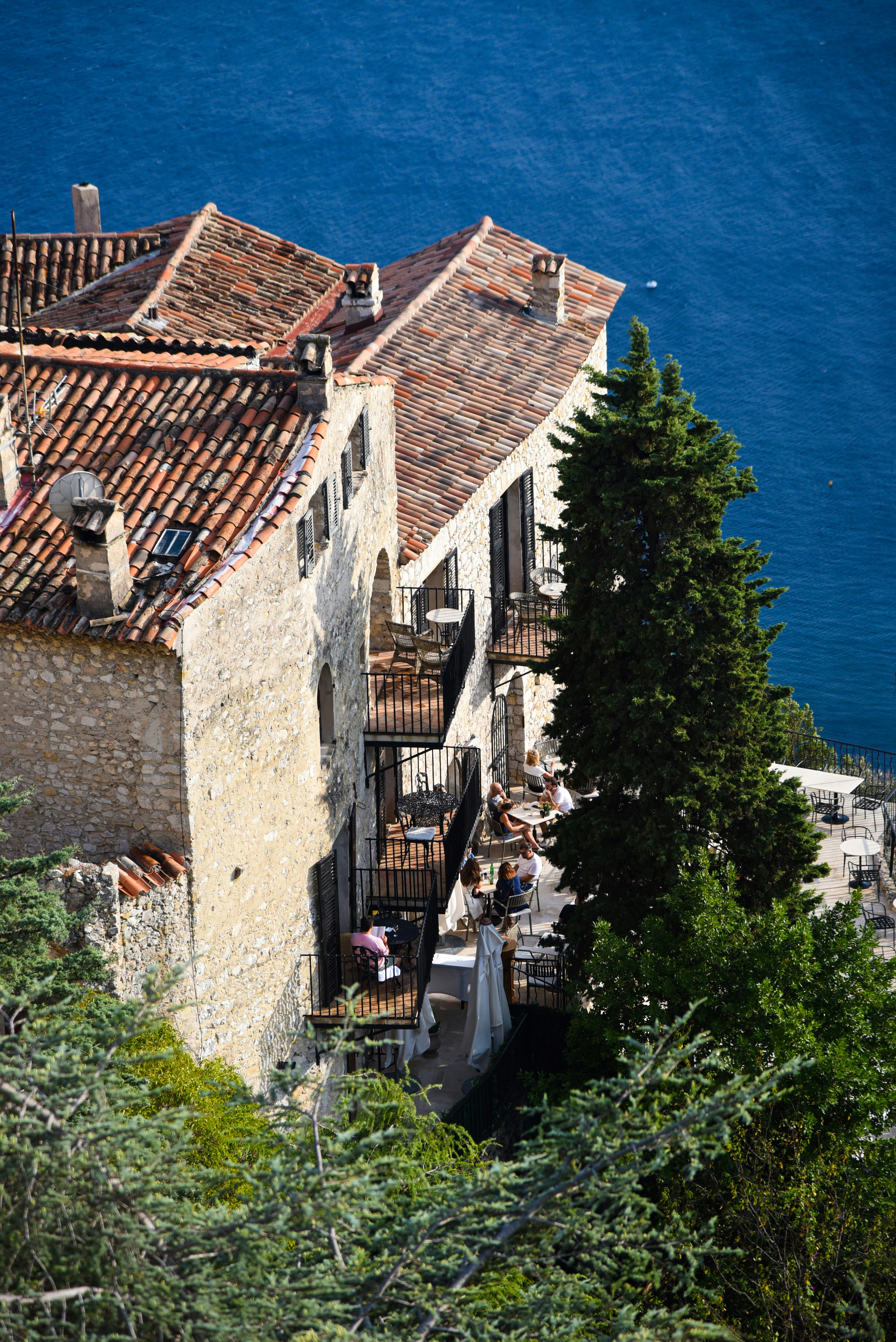 Stone buildings with balconies overlook the blue ocean.