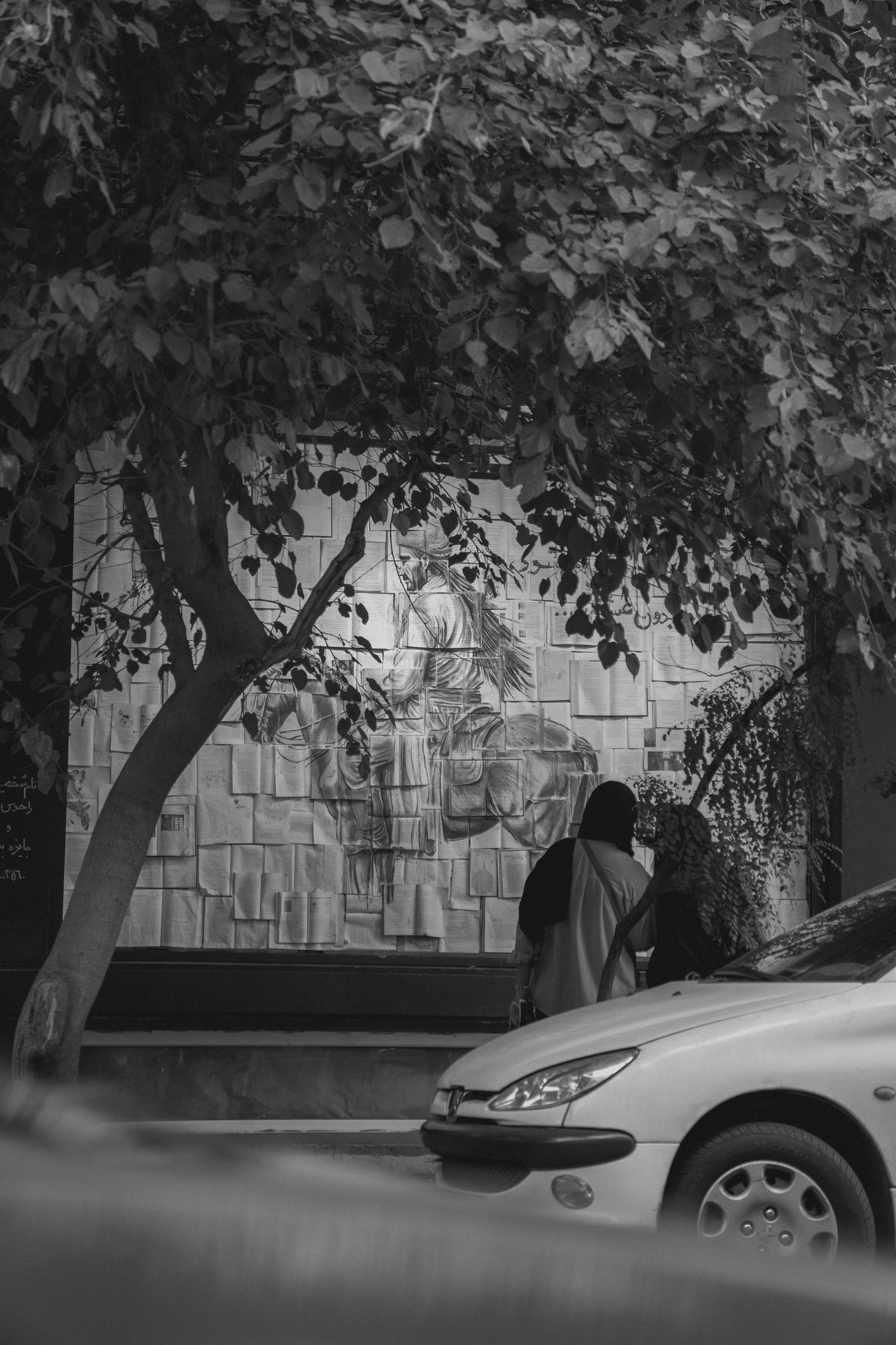 As pessoas observam um mural em uma parede atrás de um carro.