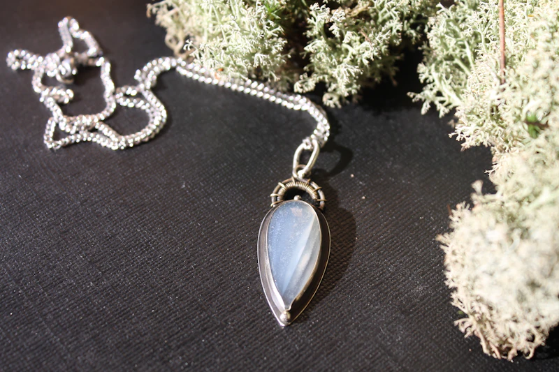 Colgante de plata con una piedra luna en forma de gota sobre liquen