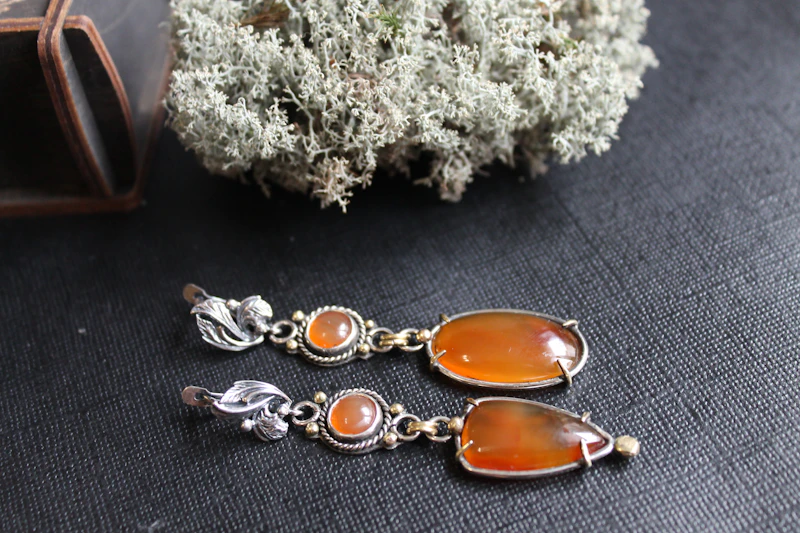 Pendientes largos de plata con cornalinas naranjas sobre fondo oscuro y liquen
