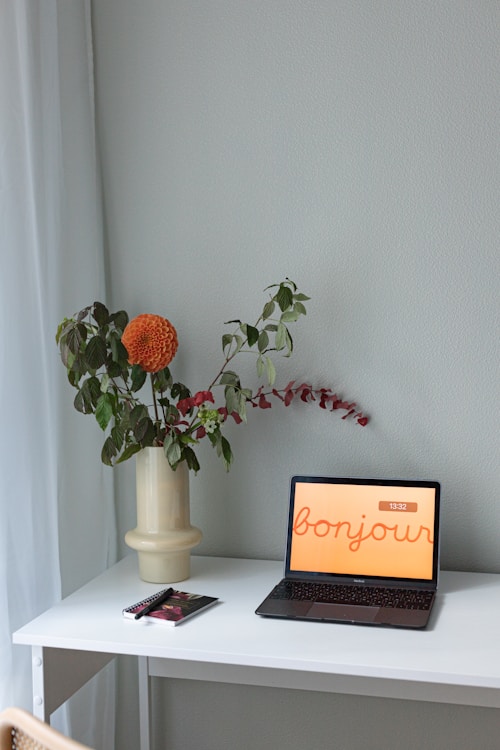 Laptop with "bonjour" on screen next to flowers.