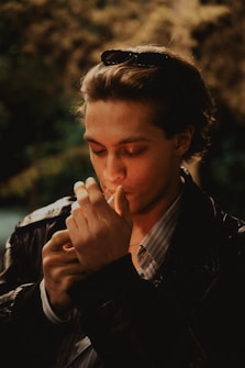Young man lighting a cigarette outdoors with sunglasses.