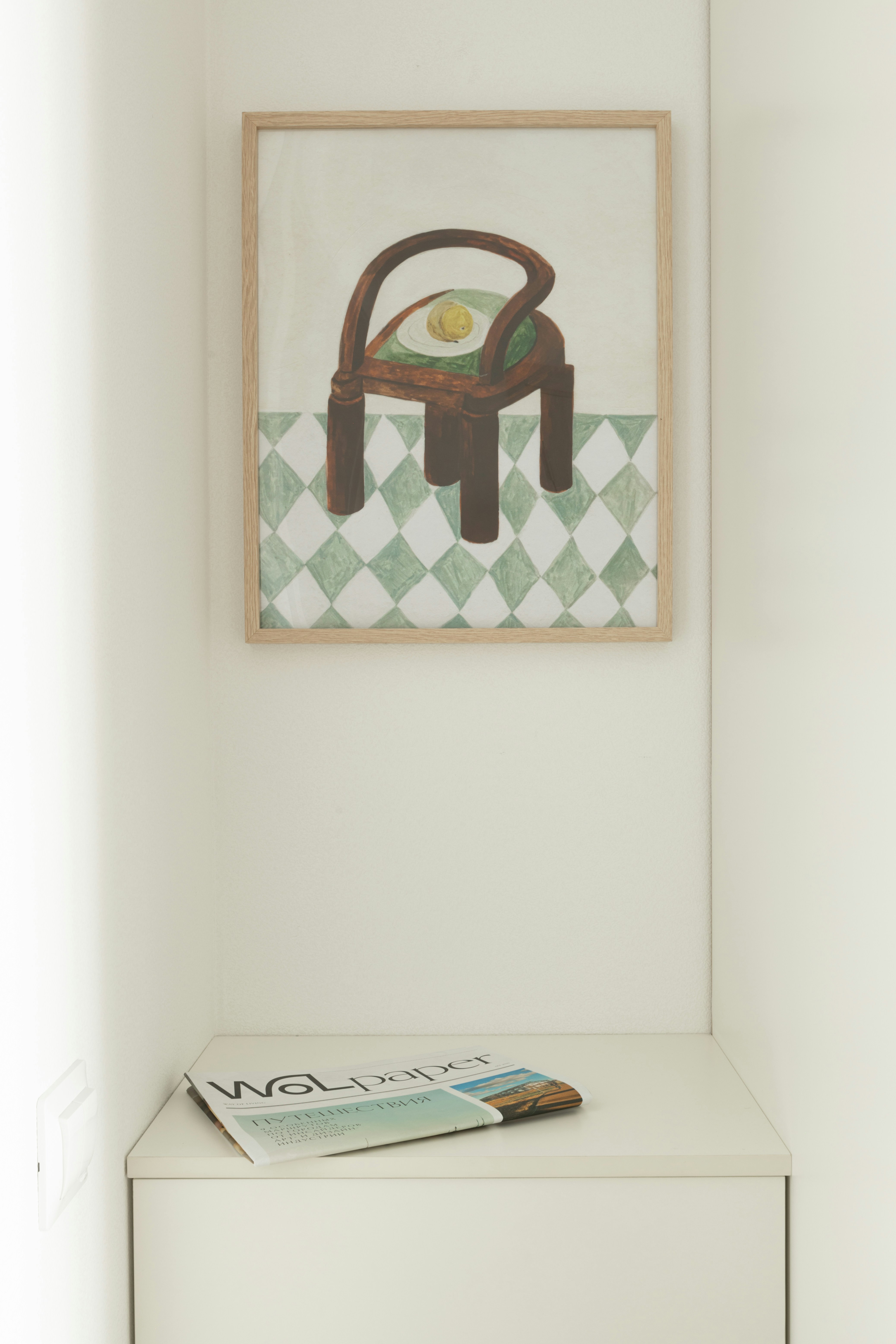 Framed artwork of a chair hangs above a magazine.