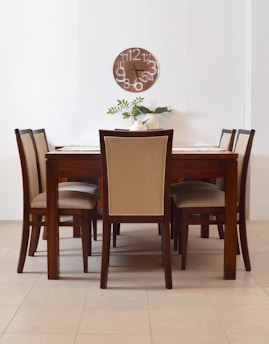 Wooden dining table with upholstered chairs and clock.
