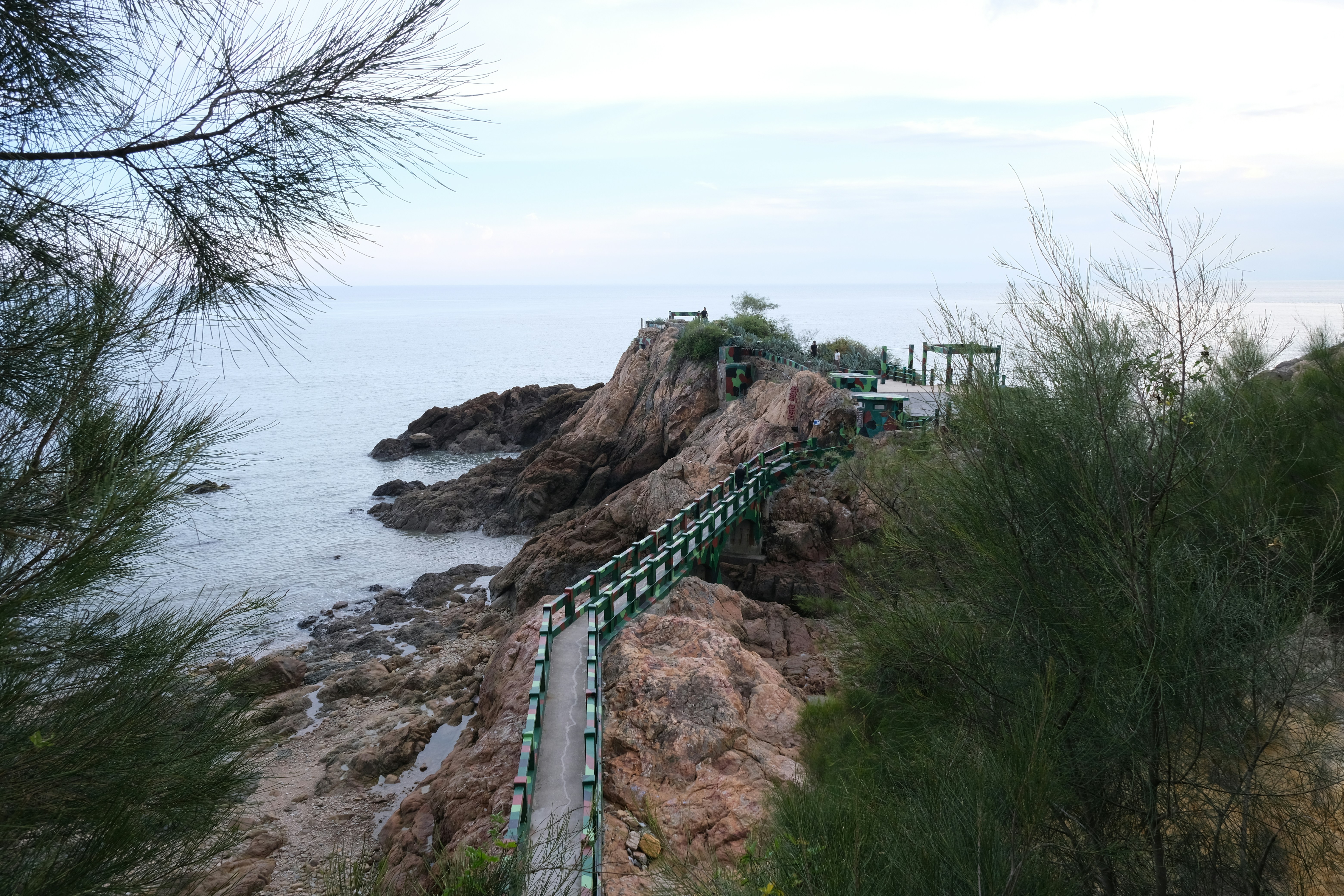 Coastal walkway leads to rocky outcrop by the sea.