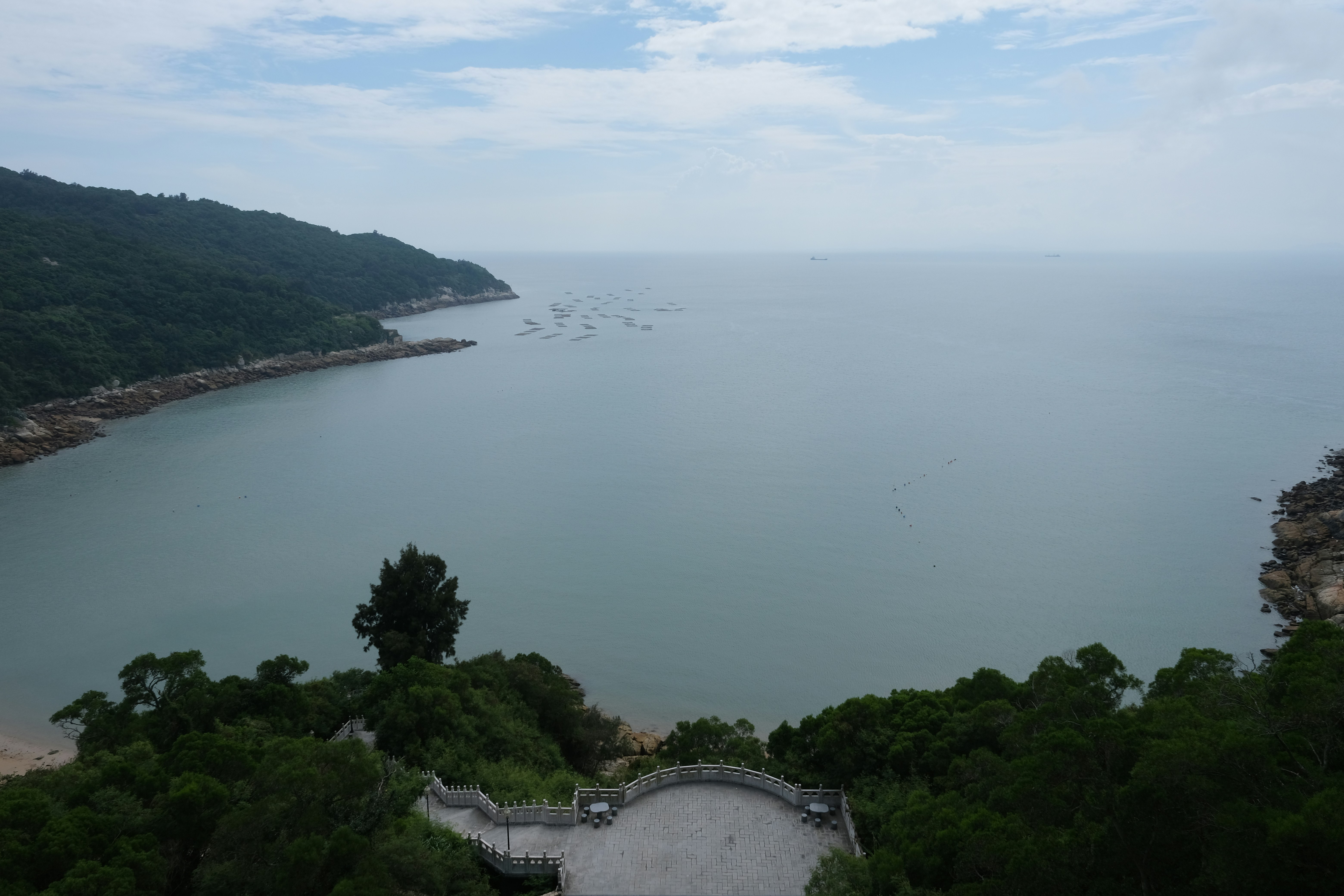 Calm sea meets lush green coastline with a scenic overlook.