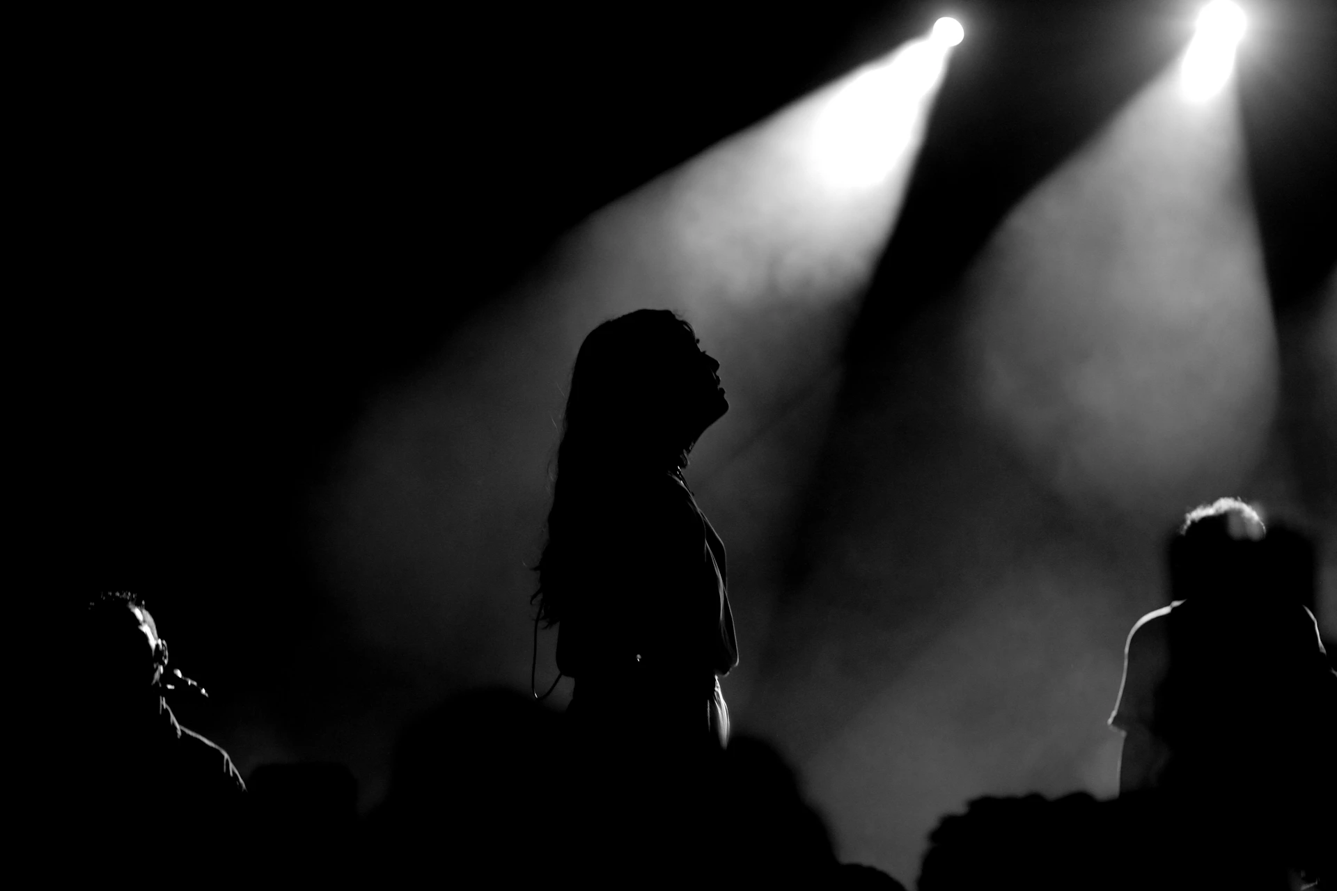 Silhouetted figures under stage spotlights at concert