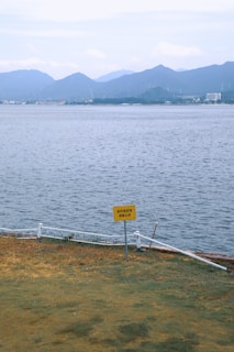 Yellow sign near water with distant mountains.
