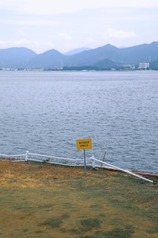 Yellow sign near water with distant mountains.