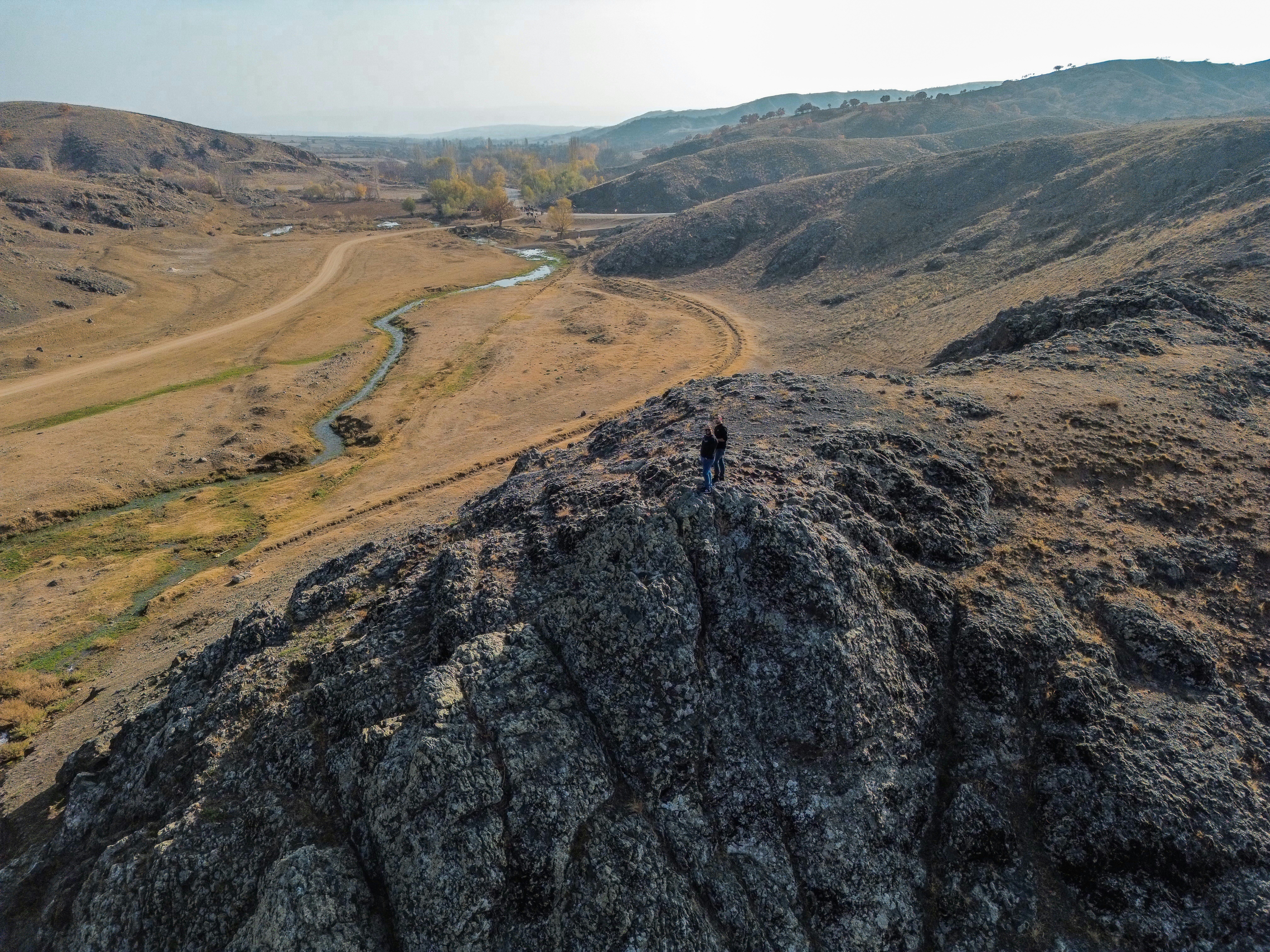 Two hikers stand atop a rocky outcrop overlooking a valley.