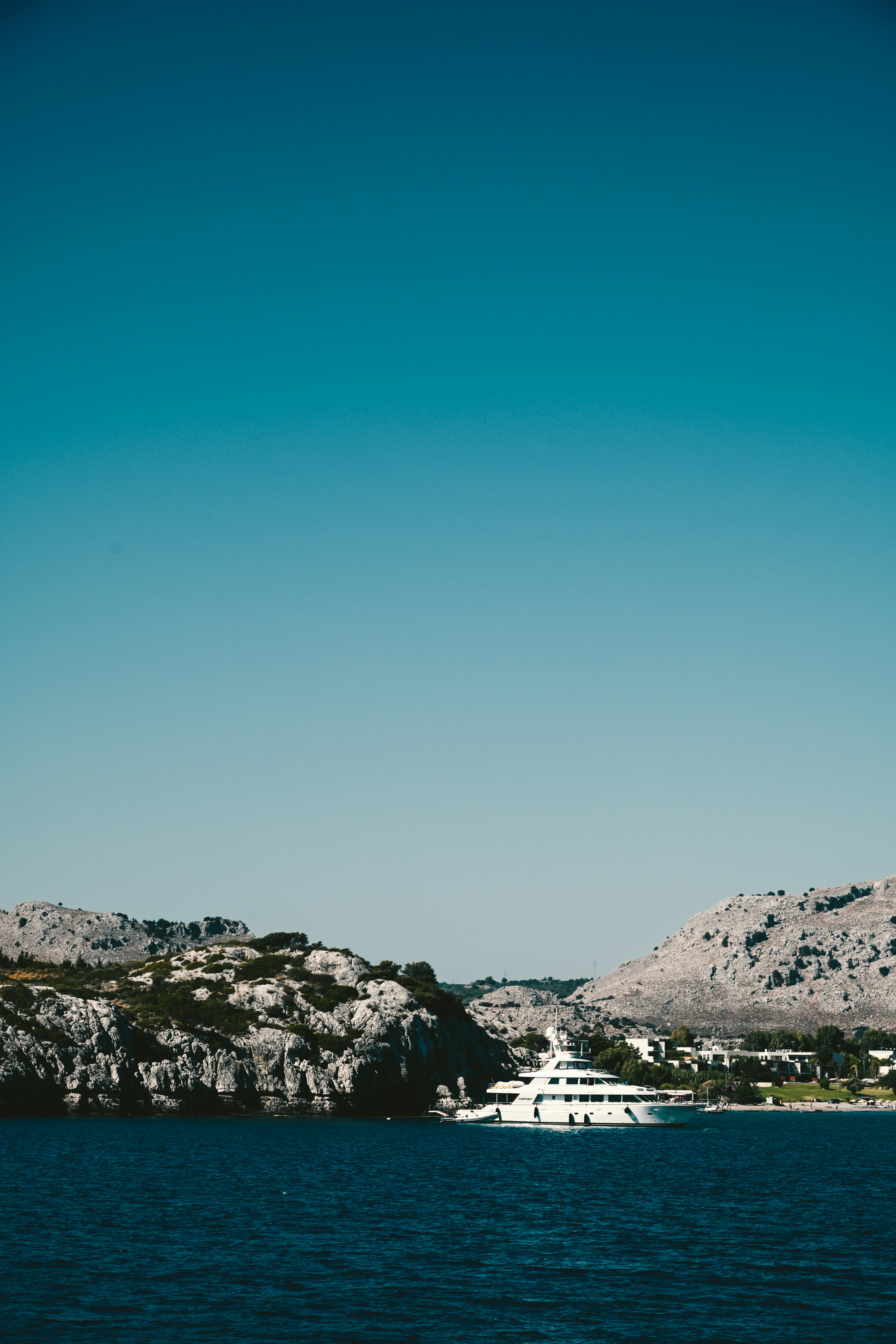 White yacht anchored near rocky coastline under clear blue sky.