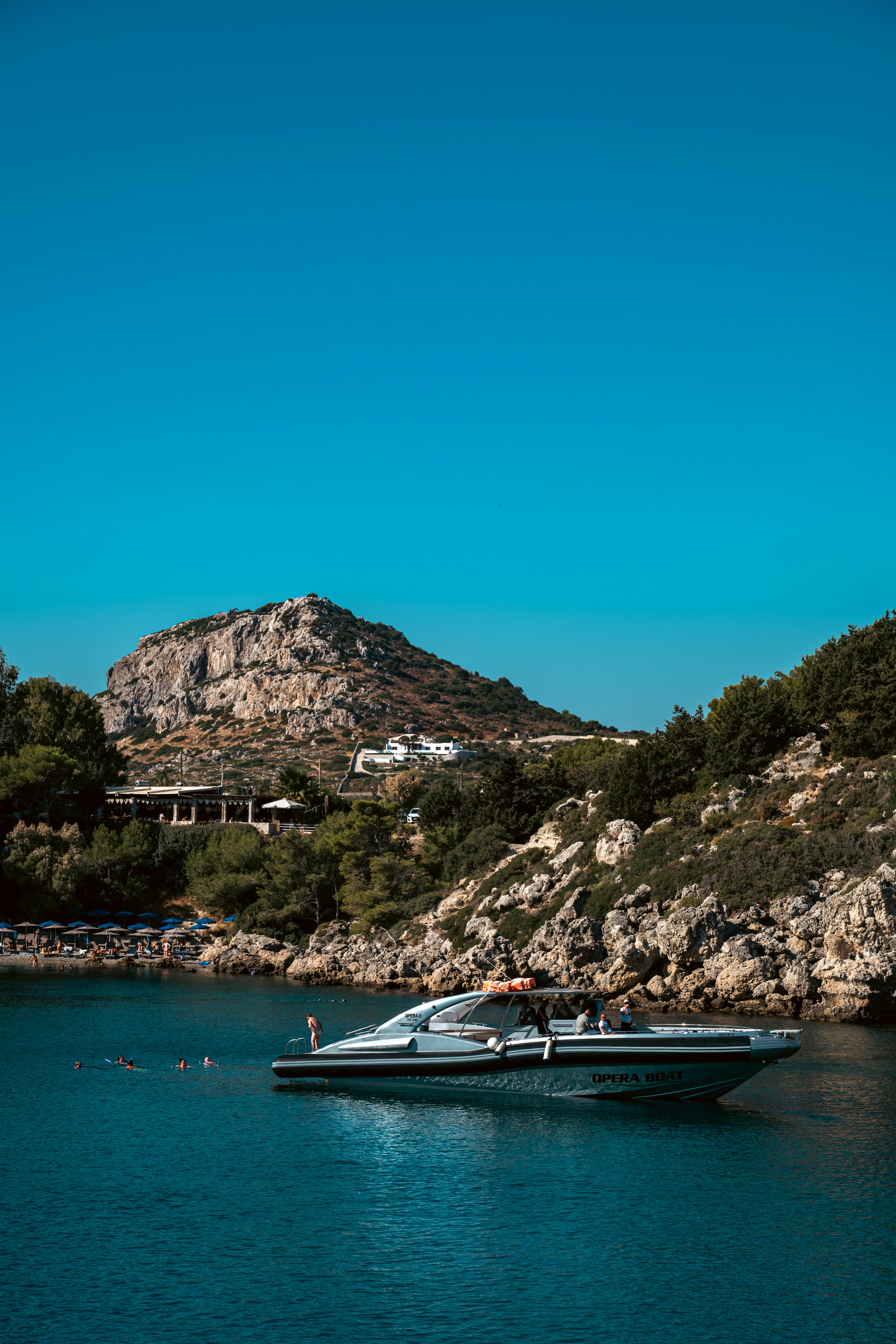 Motor yacht sails on blue water near rocky coast.