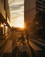Sunset illuminates people crossing a street in a city.