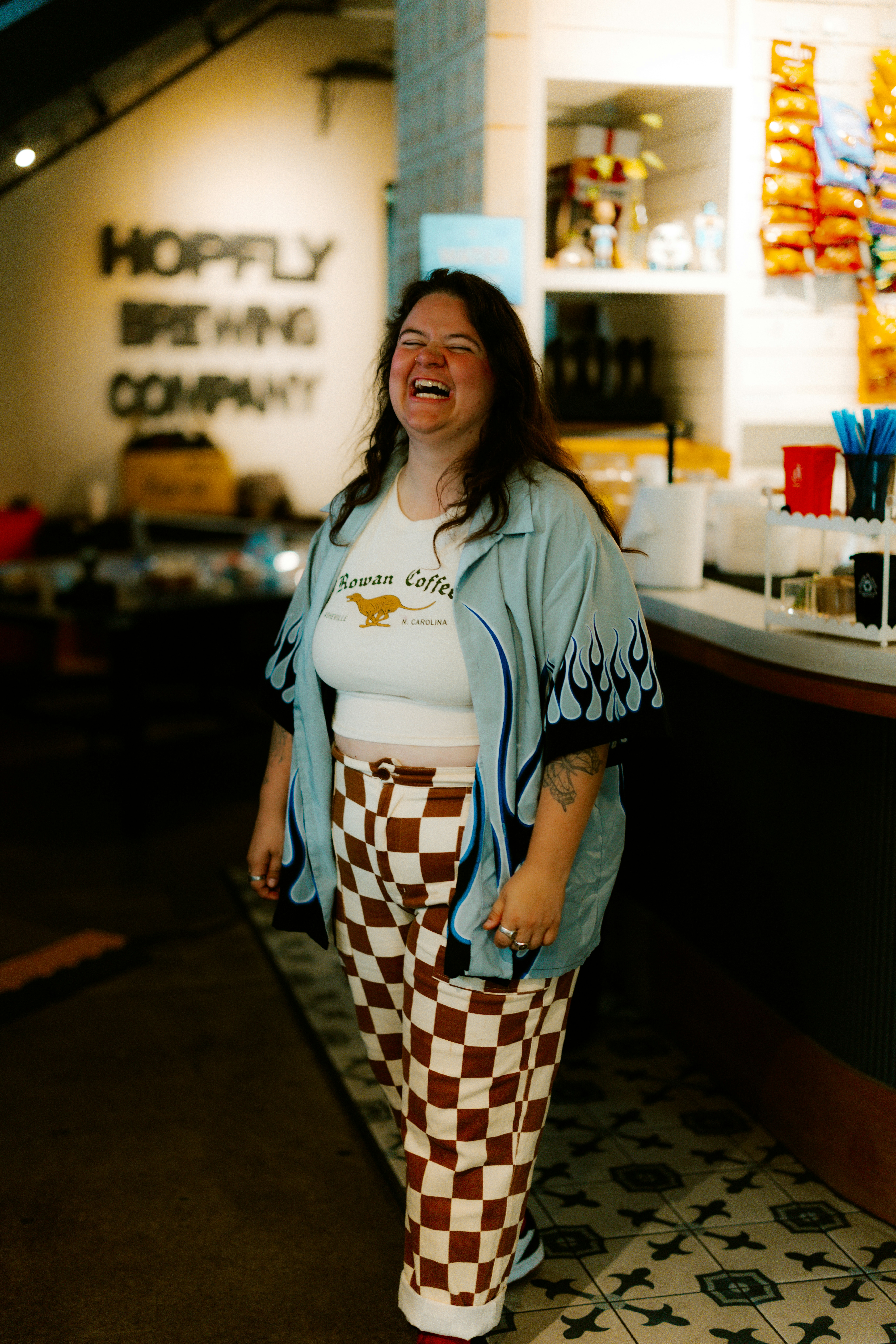 A laughing woman in checkered pants at a brewery.