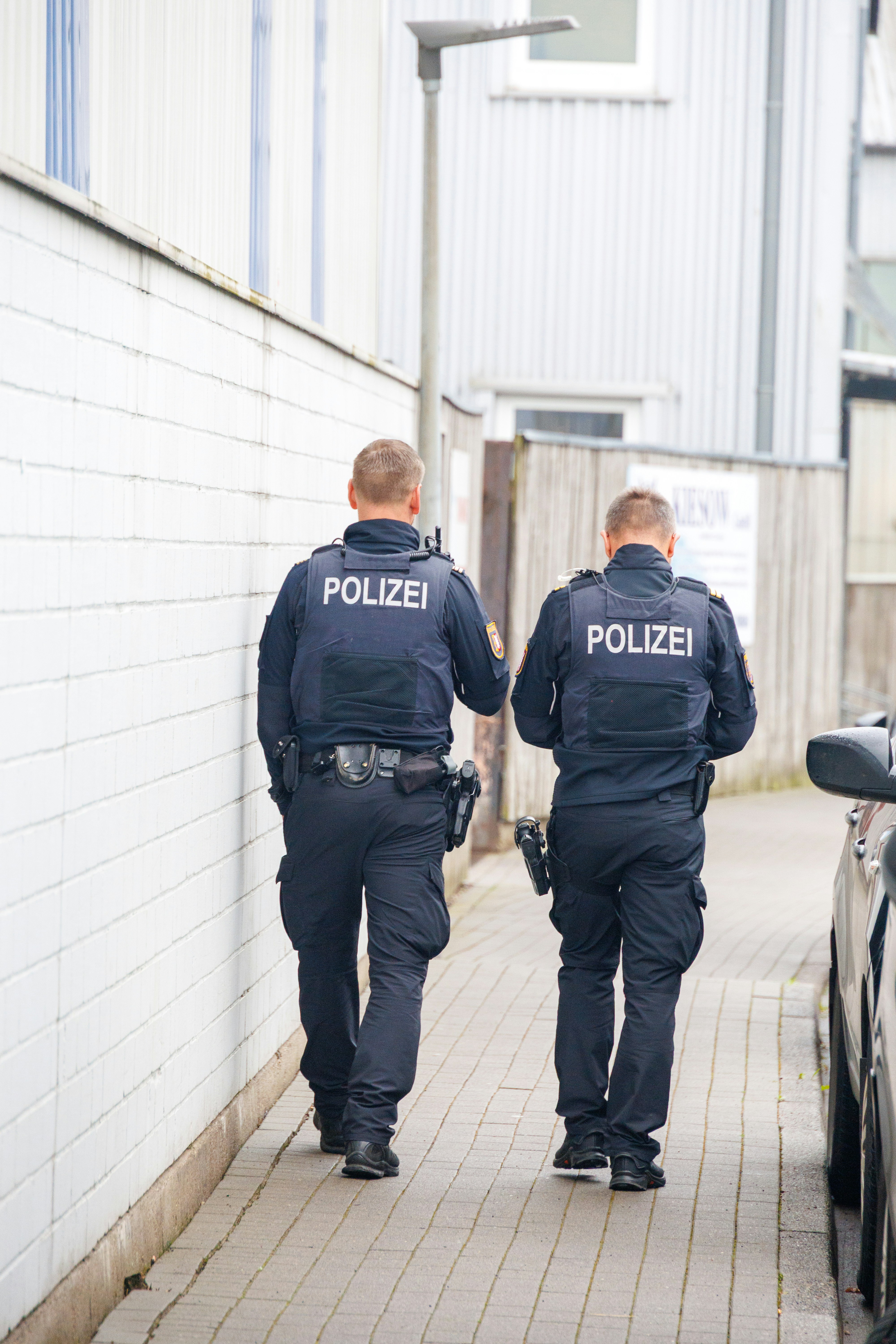 Two police officers walk down a narrow alleyway.