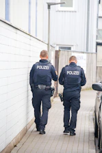 Two police officers walk down a narrow alleyway.