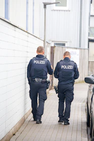 Two police officers walk down a narrow alleyway.