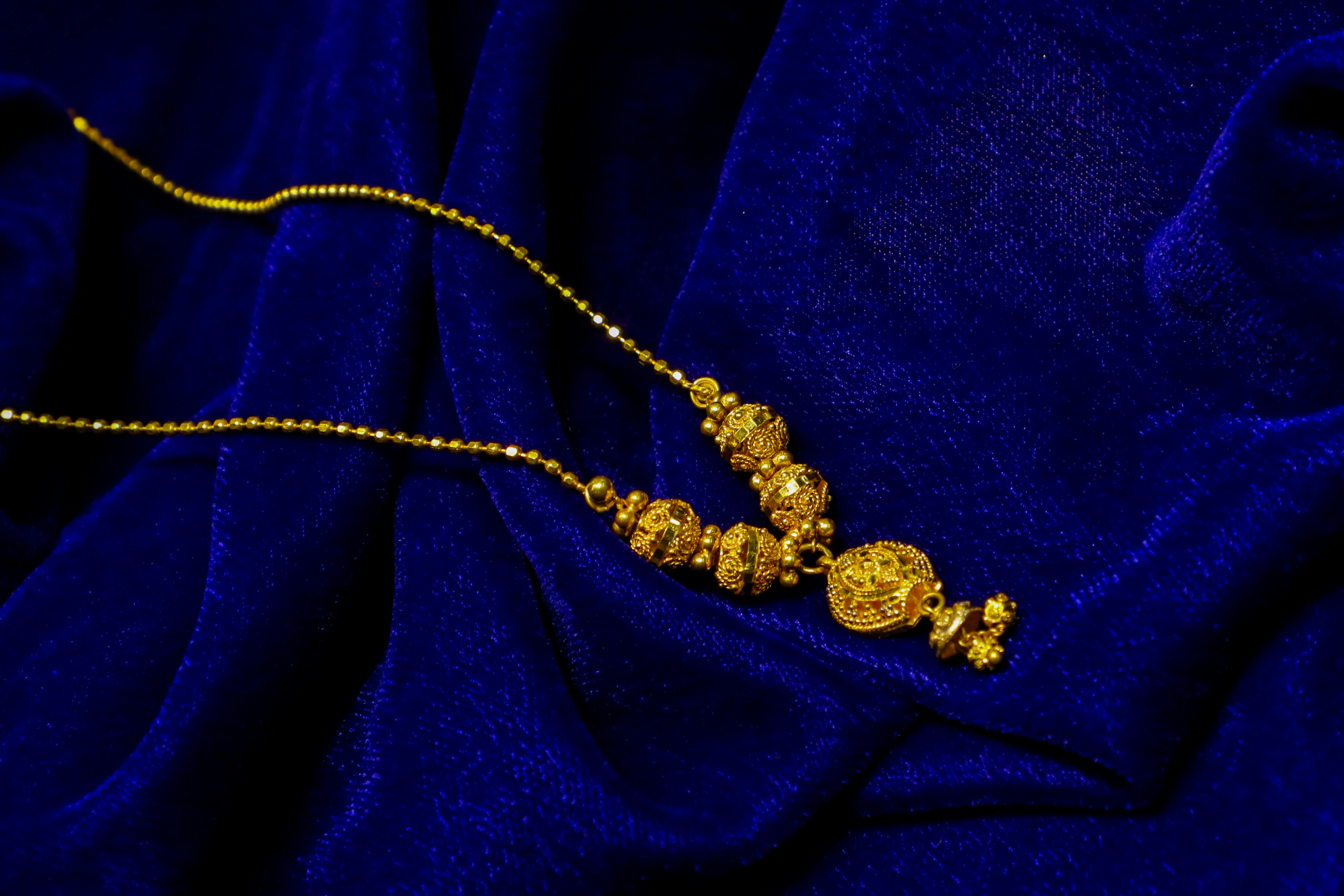 Gold necklace with intricate bead details on blue velvet