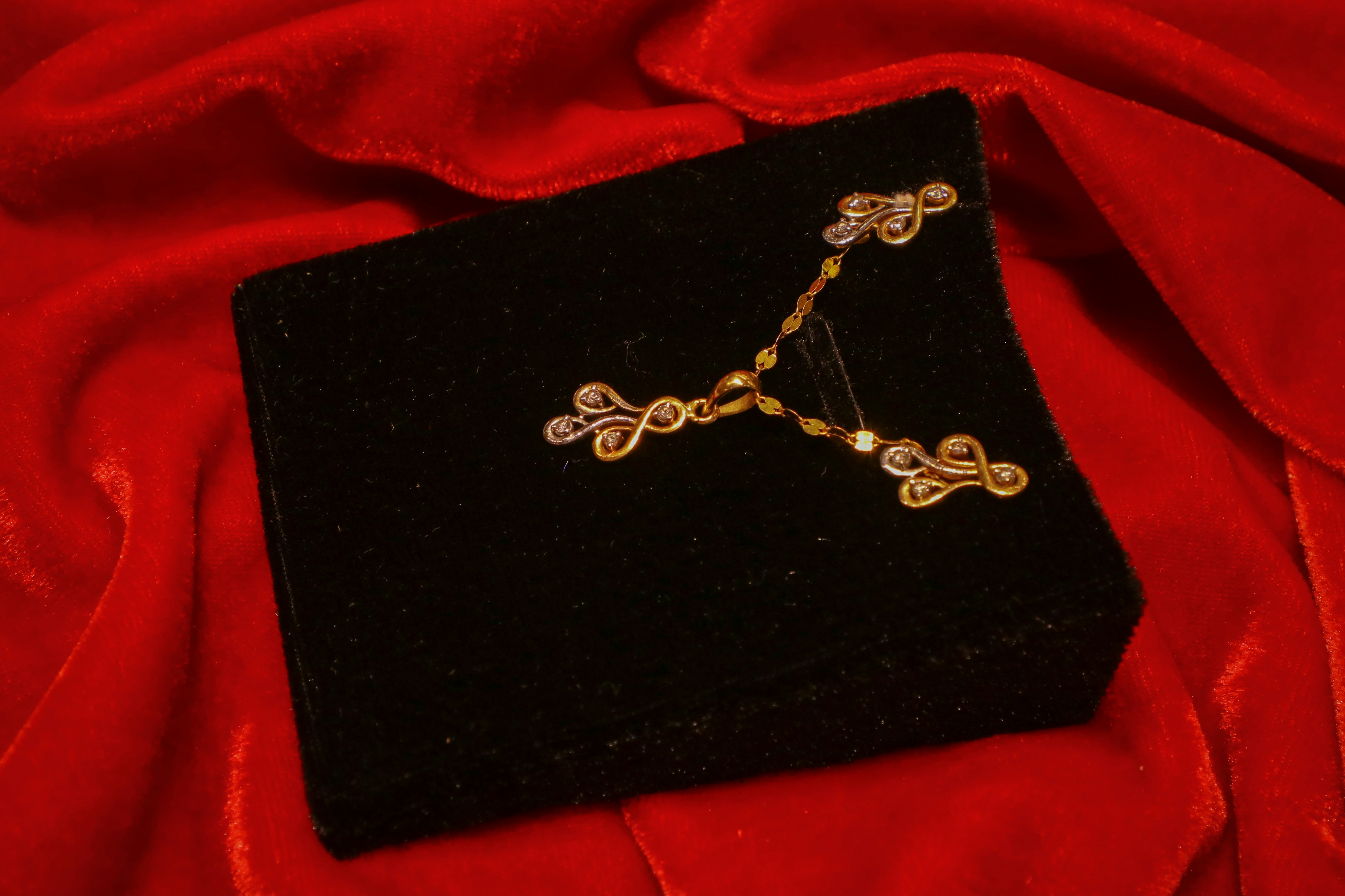 A delicate gold and diamond-studded jewelry set with a pendant and matching earrings, elegantly displayed on a black velvet box over a luxurious red fabric background.
