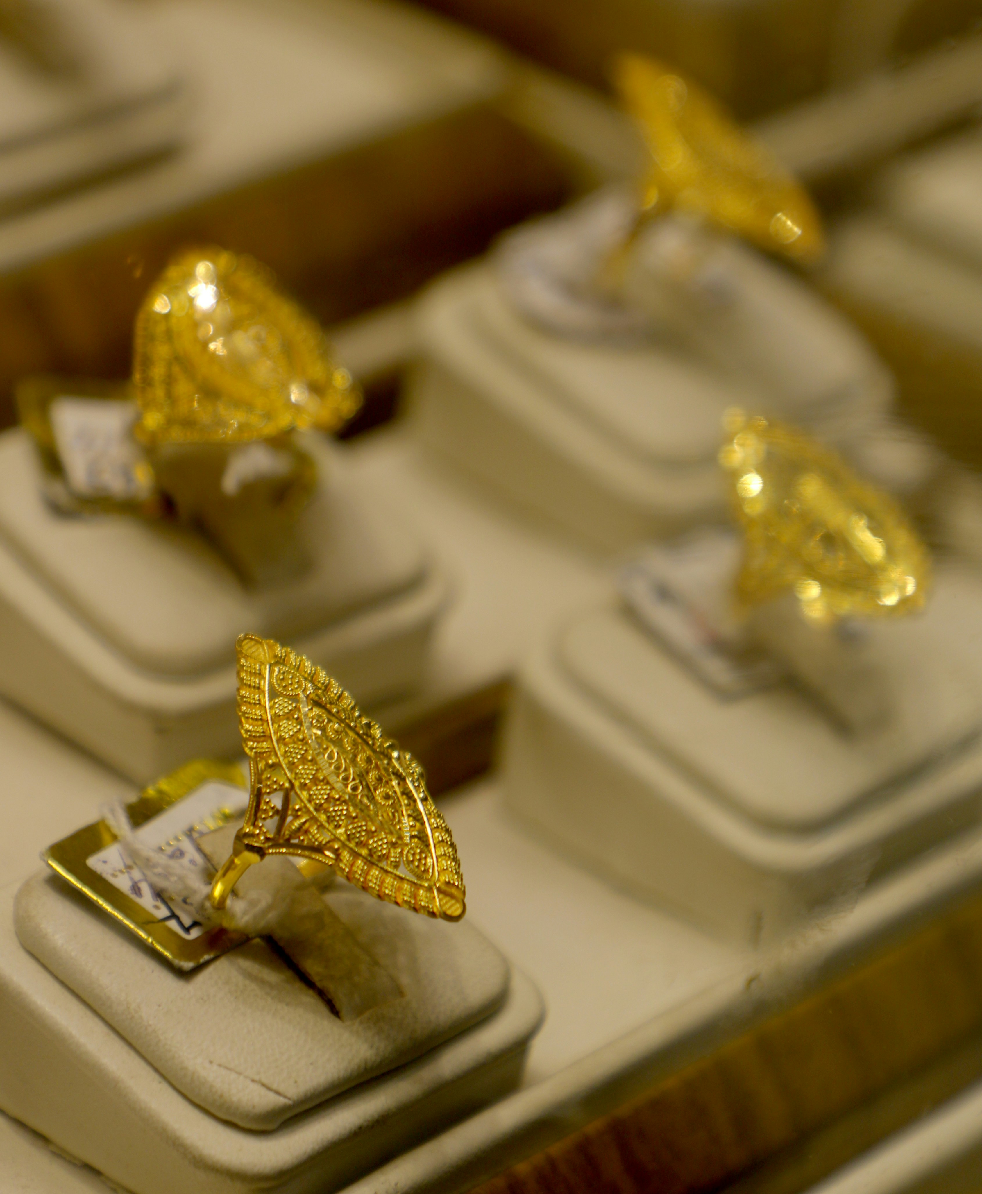 A collection of ornate gold rings with intricate designs displayed on cushioned stands in a jewelry store, highlighting their craftsmanship, elegance, and luxurious appeal.