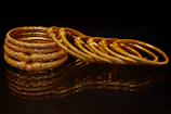 A stack of ornate gold bangles on a dark surface.