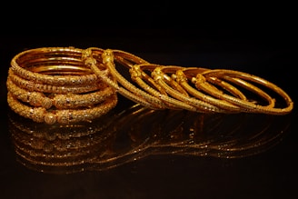 A stack of ornate gold bangles on a dark surface.