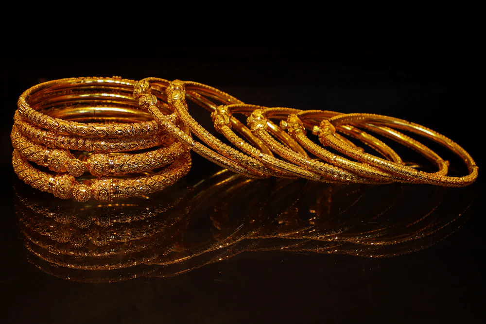 Stack of ornate gold bangle bracelets on a dark surface