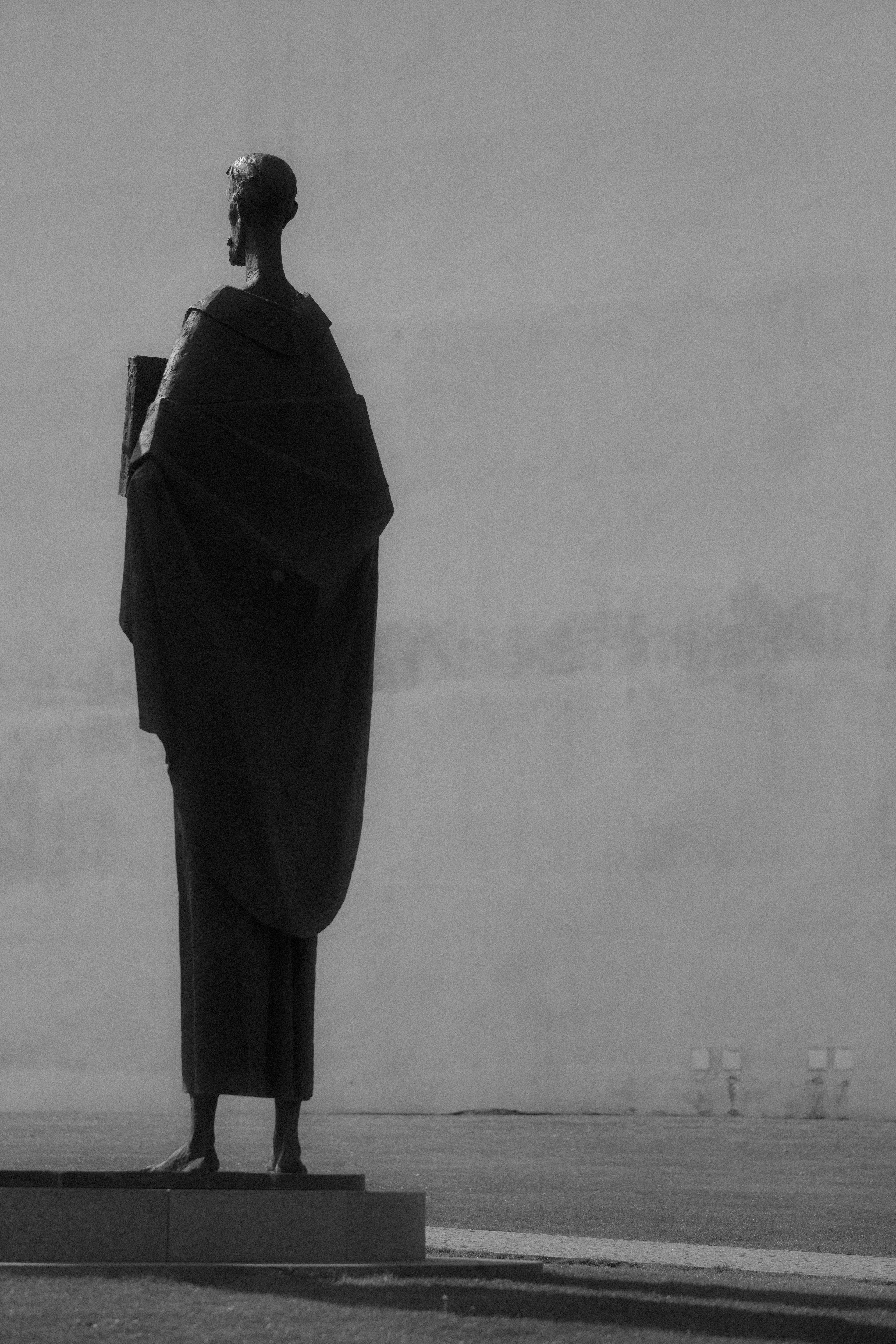 Statue of a robed figure holding a book outdoors.