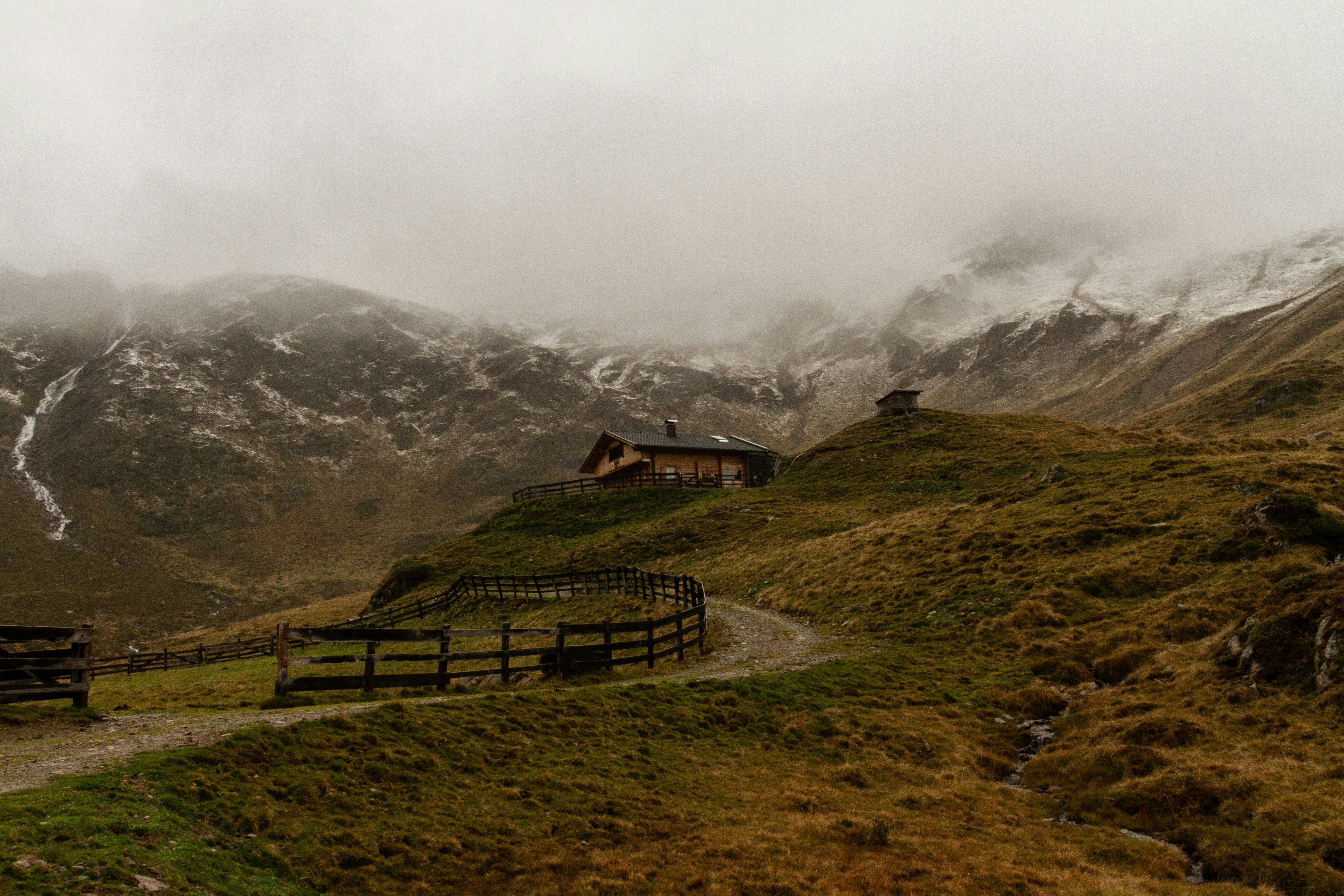 Foggy mountain landscape with a small cabin and fence.