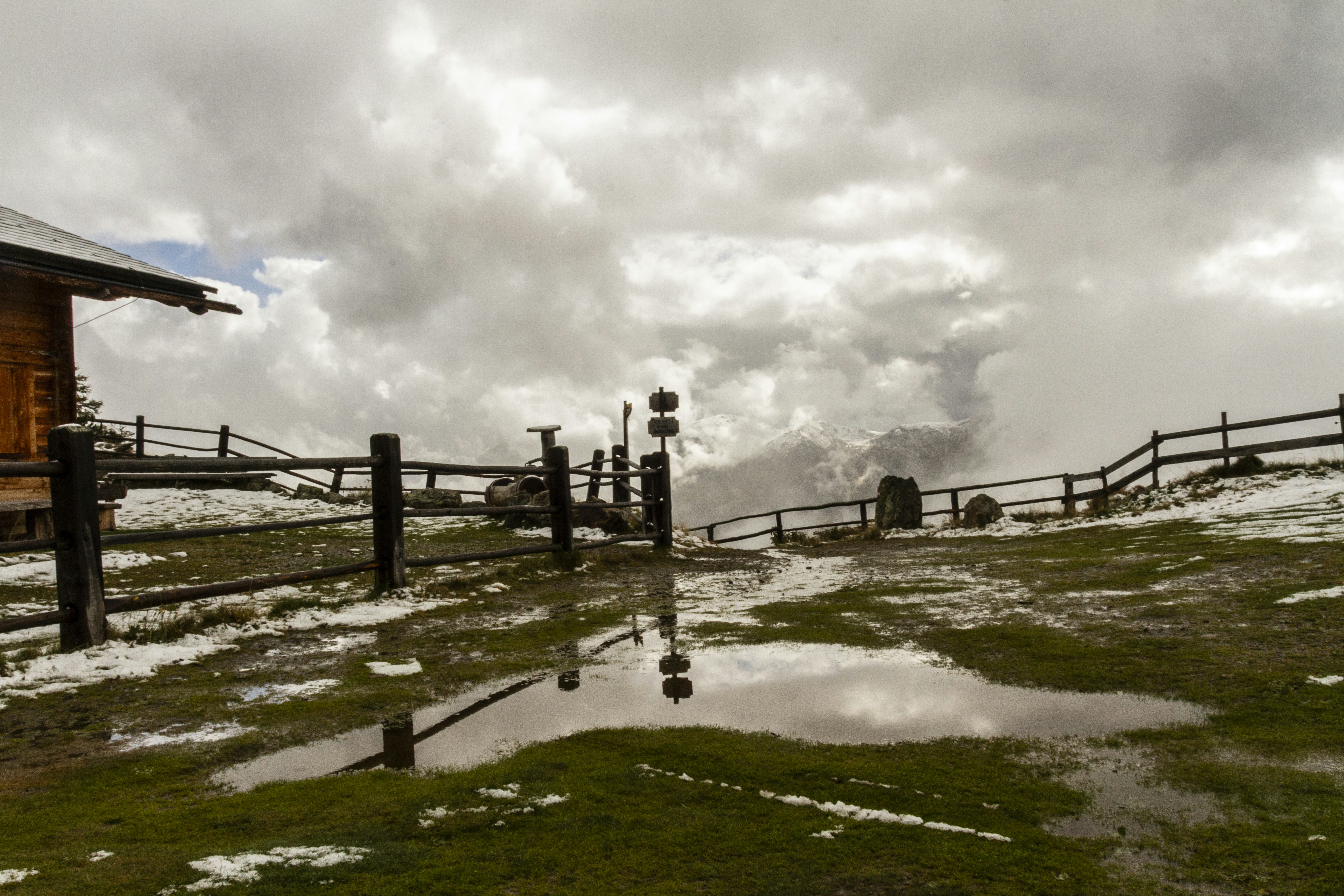 Wooden cabin and fence with snowy ground and puddles.