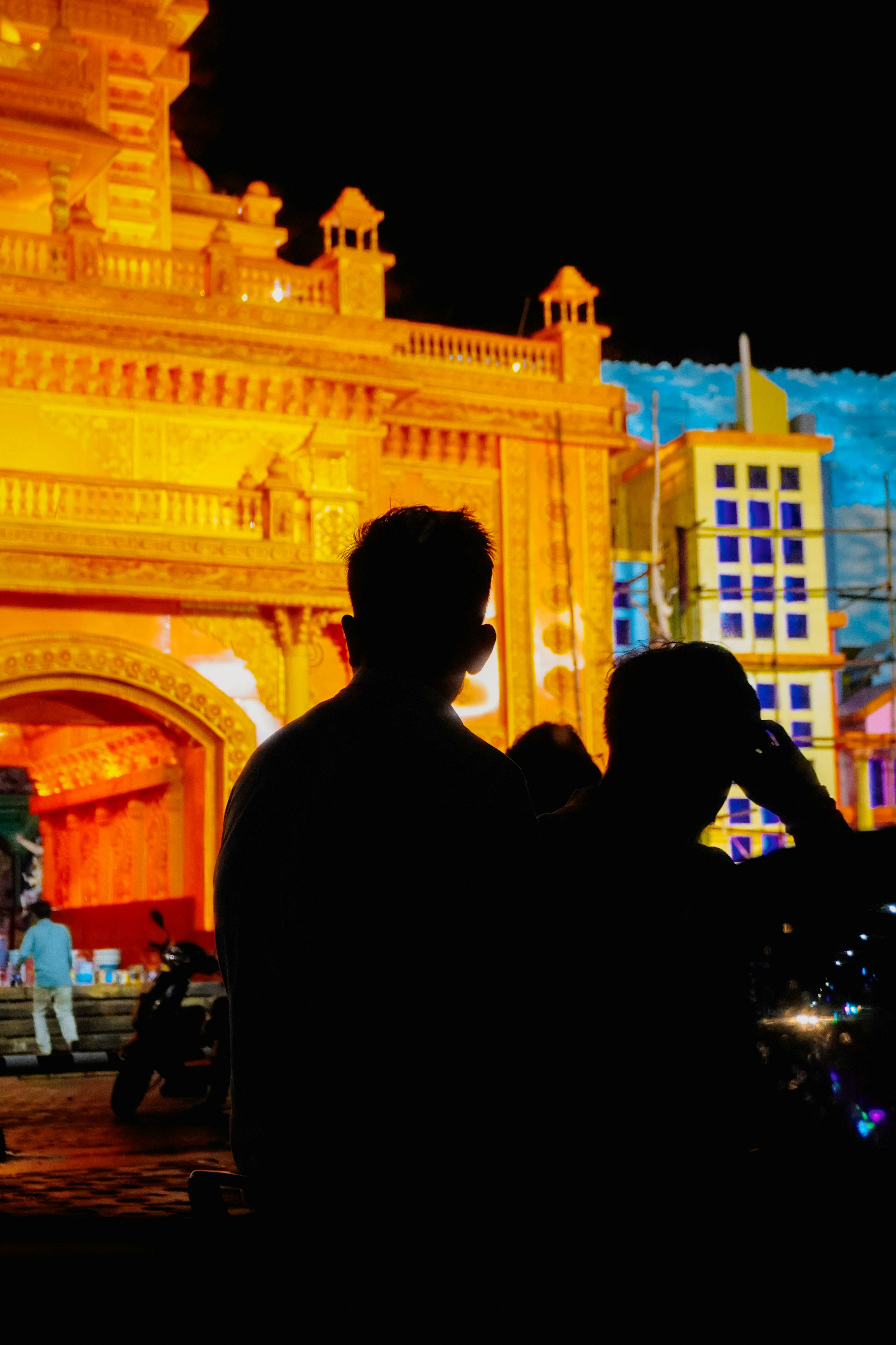 Silhouetted figures against illuminated festival decorations